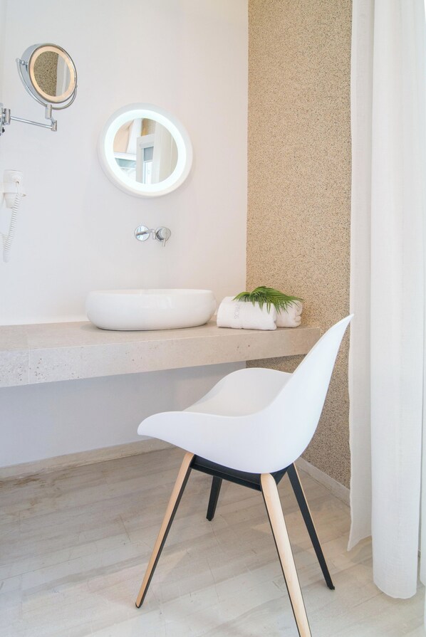 Un baño moderno con un lavamanos blanco, un espejo redondo y una silla blanca.