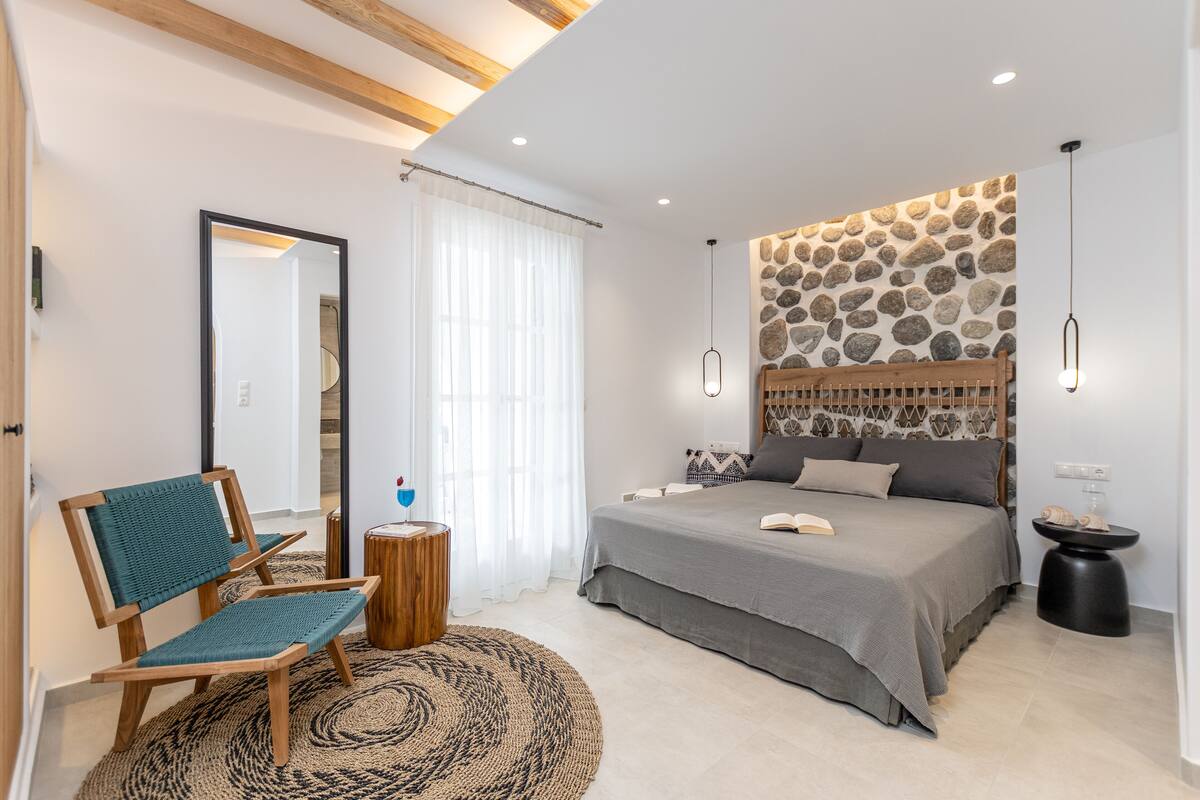 Une chambre avec un lit, une chaise, un miroir et un mur en pierre.