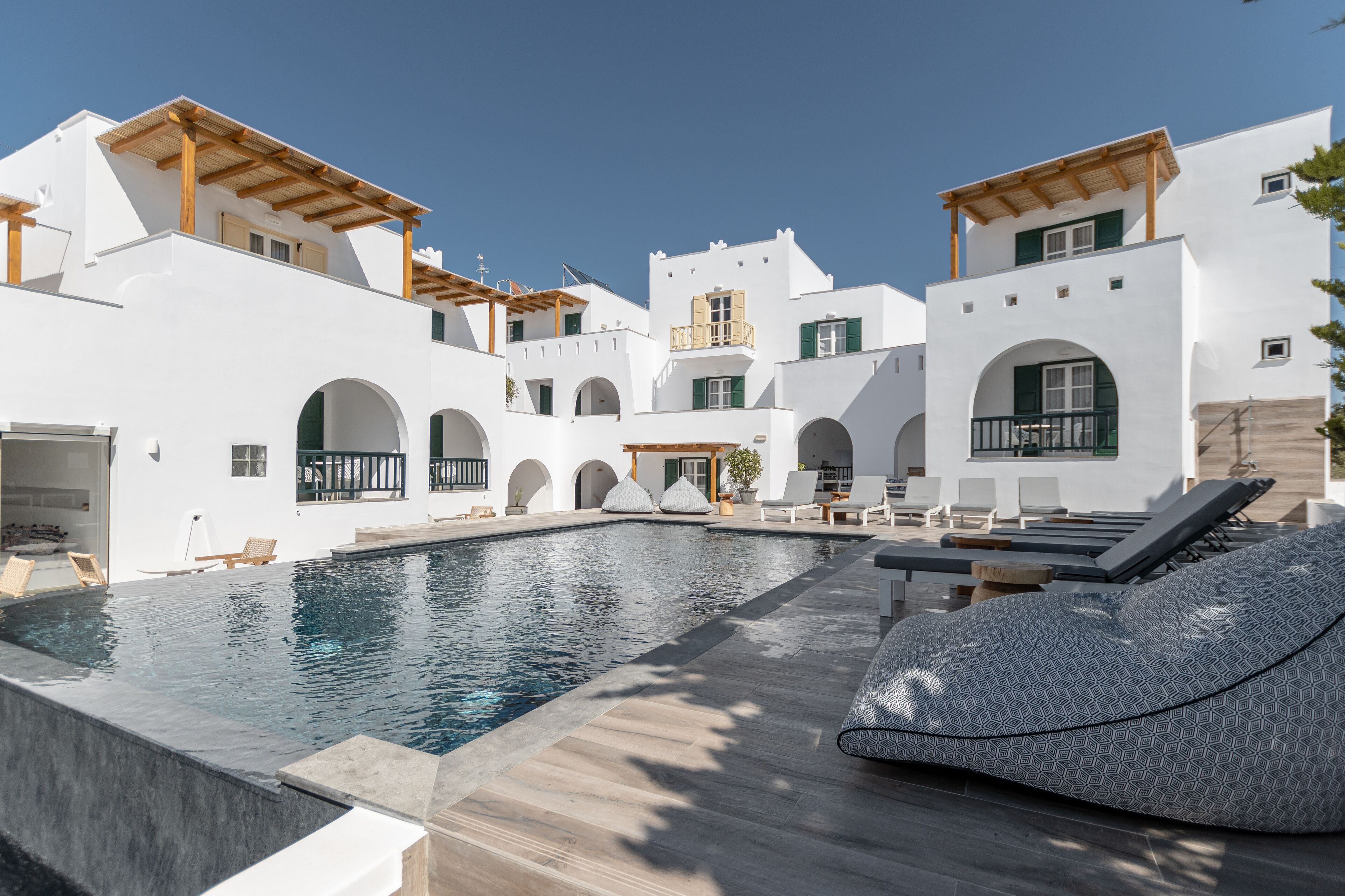 A modern pool area with white buildings, wooden pergolas, and lounge chairs.