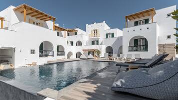 A modern pool area with white buildings, wooden pergolas, and lounge chairs.