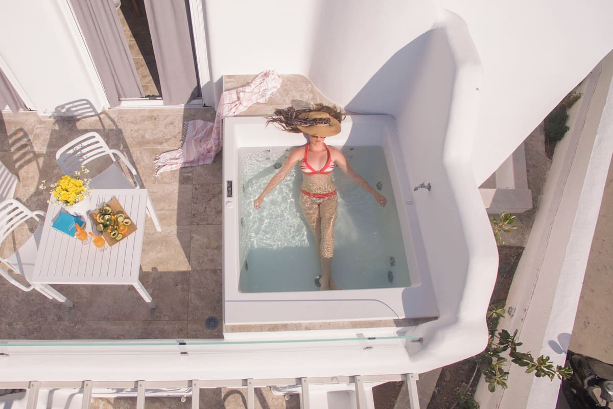 Un bain à remous avec une personne à l’intérieur, une table avec un vase de fleurs et des chaises blanches.