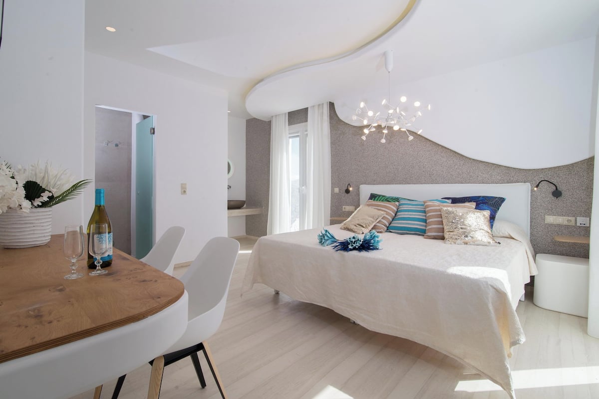 Une chambre à coucher moderne avec un plafond incurvé, un lit agrémenté de plusieurs oreillers, une table de chevet et une petite lampe de chevet.