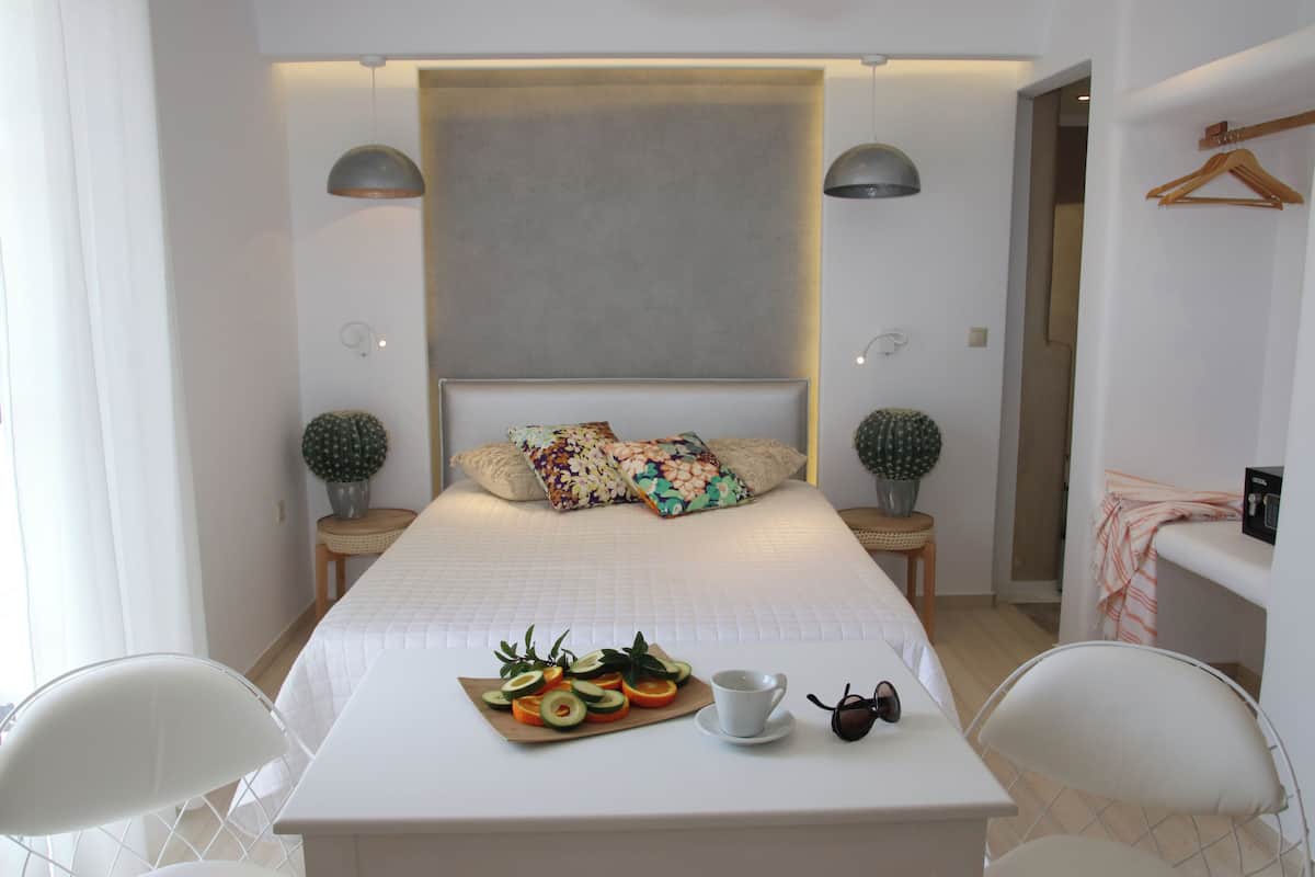 Une chambre d’hôtel moderne avec un grand lit, un plateau de petit-déjeuner avec des fruits et une tasse, ainsi que deux tables de chevet avec des lampes.