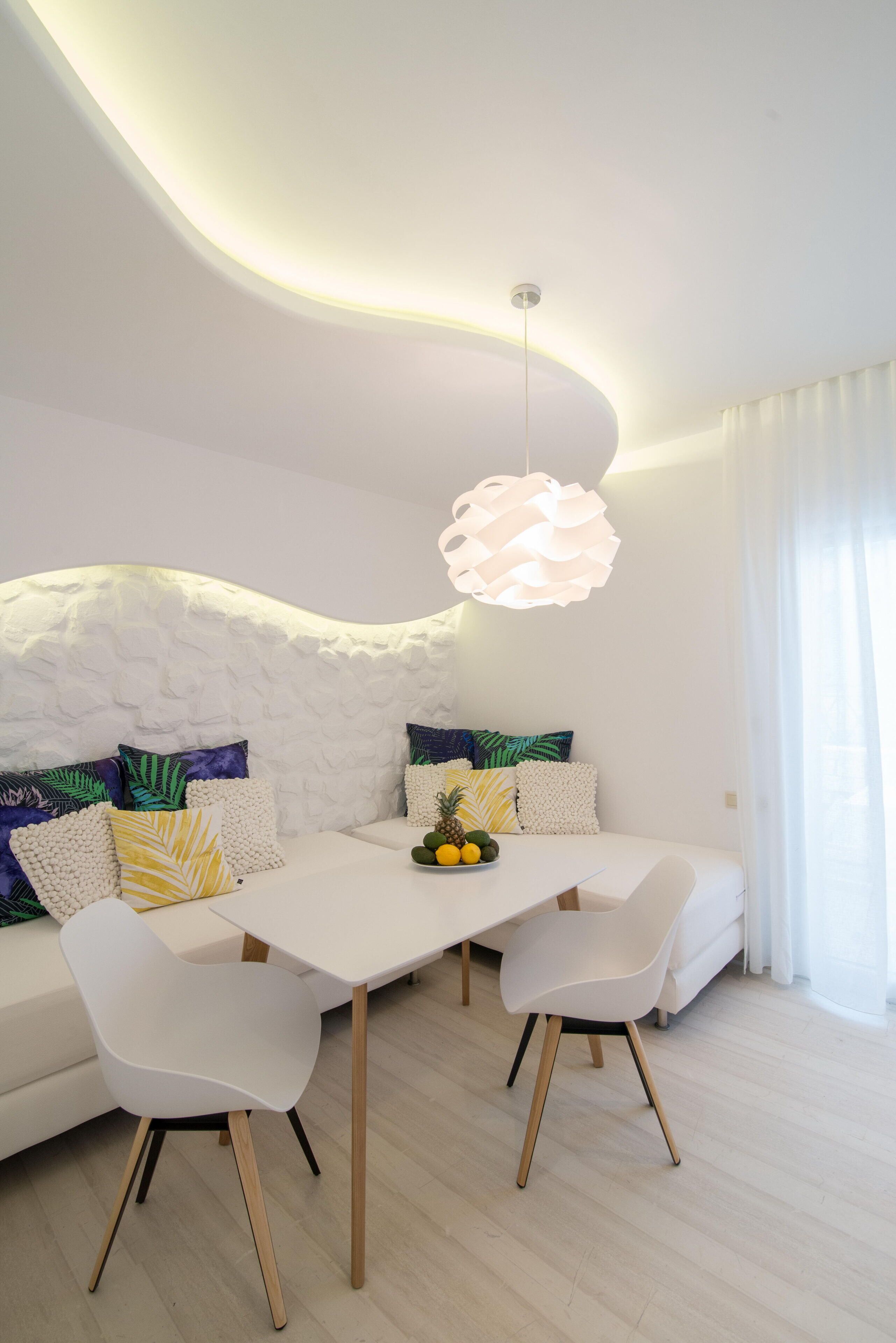 A modern living room with a white sofa, a dining table, and a unique ceiling design.