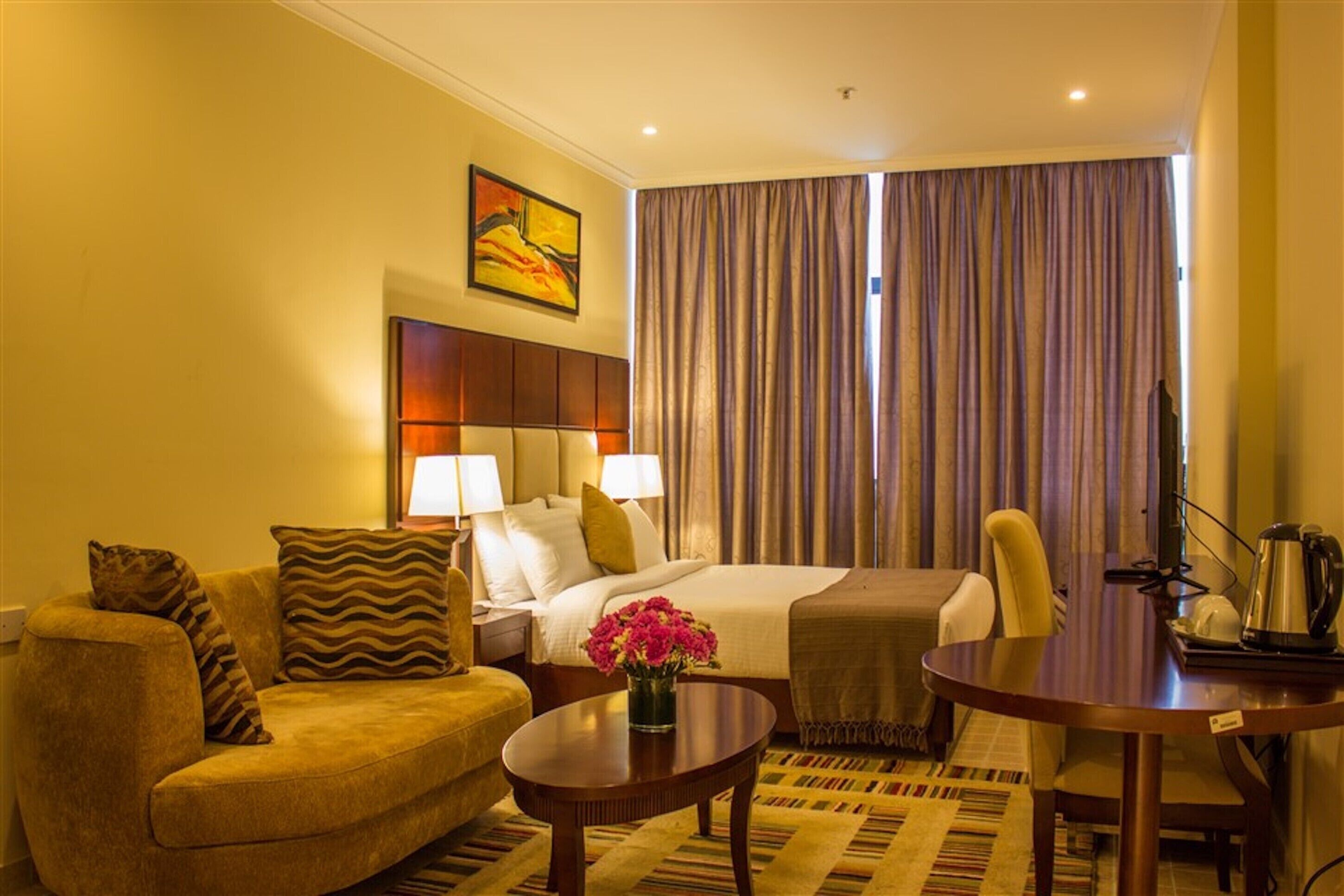 A hotel room with a bed, a sofa, a coffee table, and a dining table.