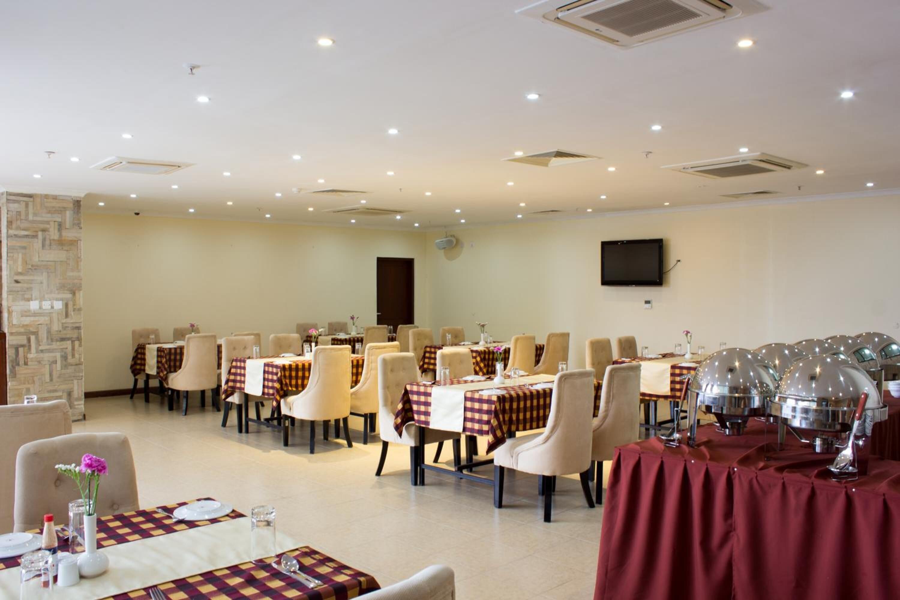 Un comedor con varias mesas y sillas, un televisor montado en la pared y una mesa de buffet con platos cubiertos.