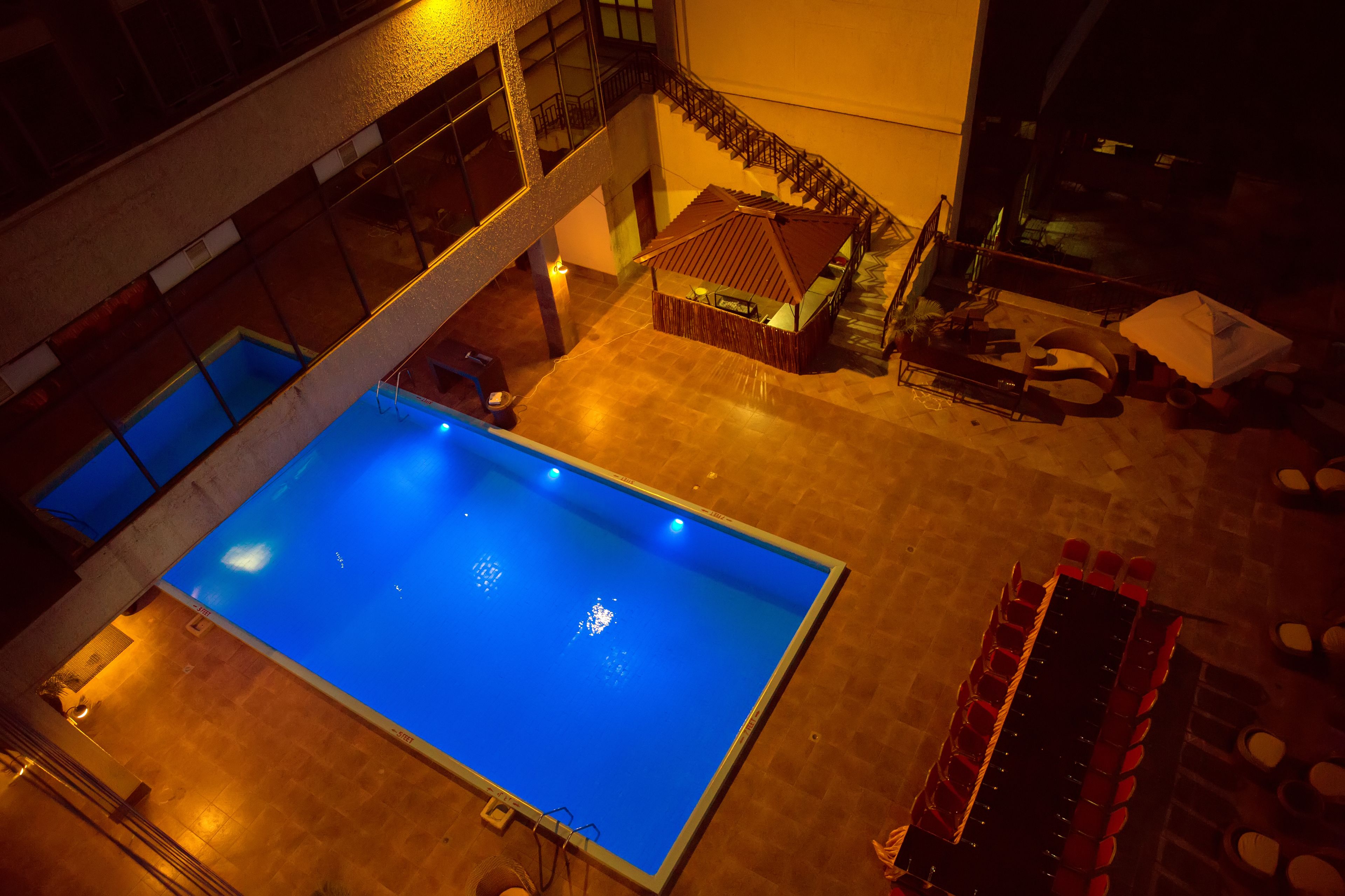 A rooftop pool with a view of the cityscape, a small building with a tiled roof, and a staircase leading to an upper level.