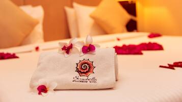 A neatly made bed with a towel and flowers, a lamp, and a bedspread.