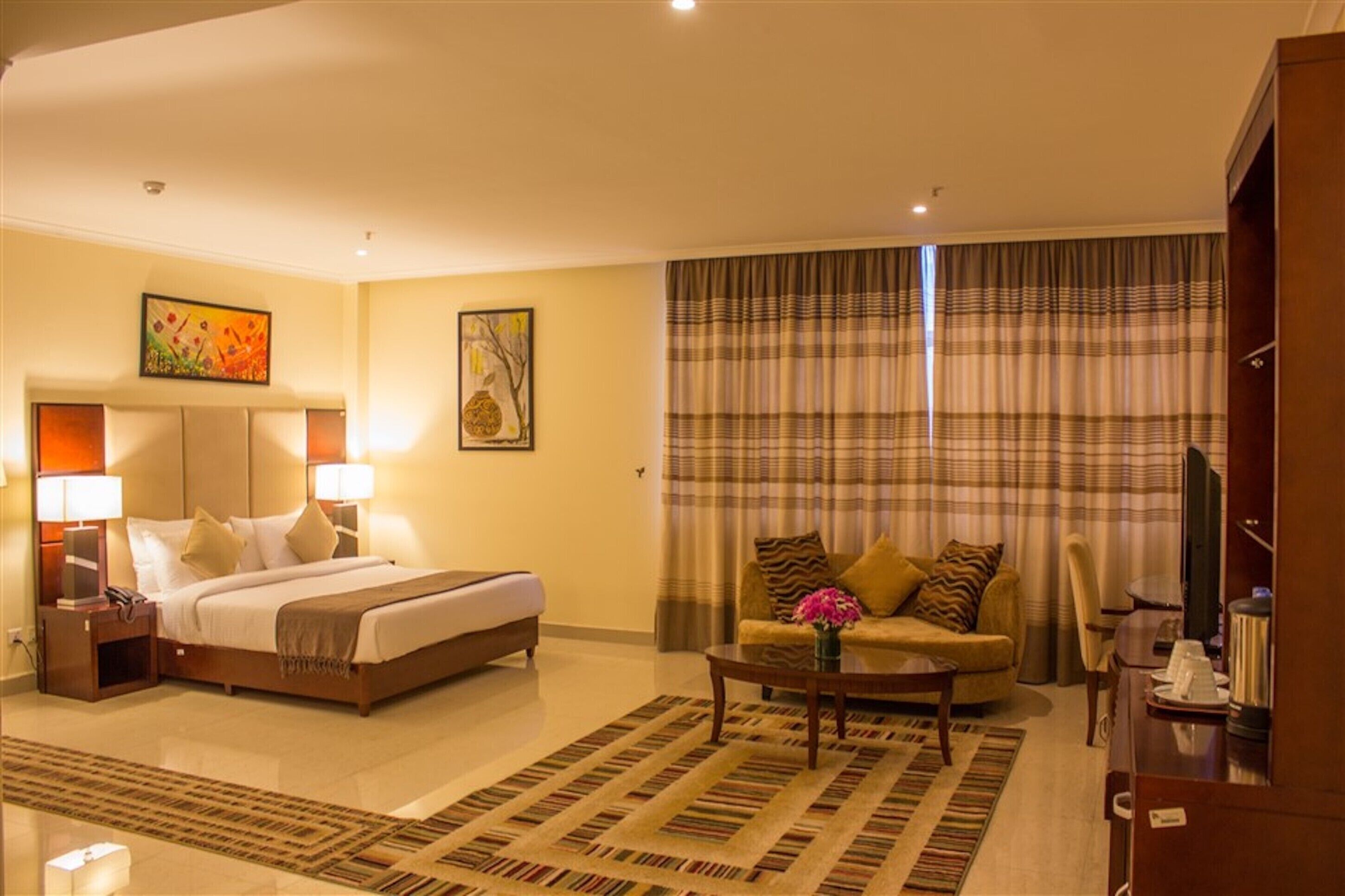 A hotel room with a bed, a sofa, a coffee table, and a television.
