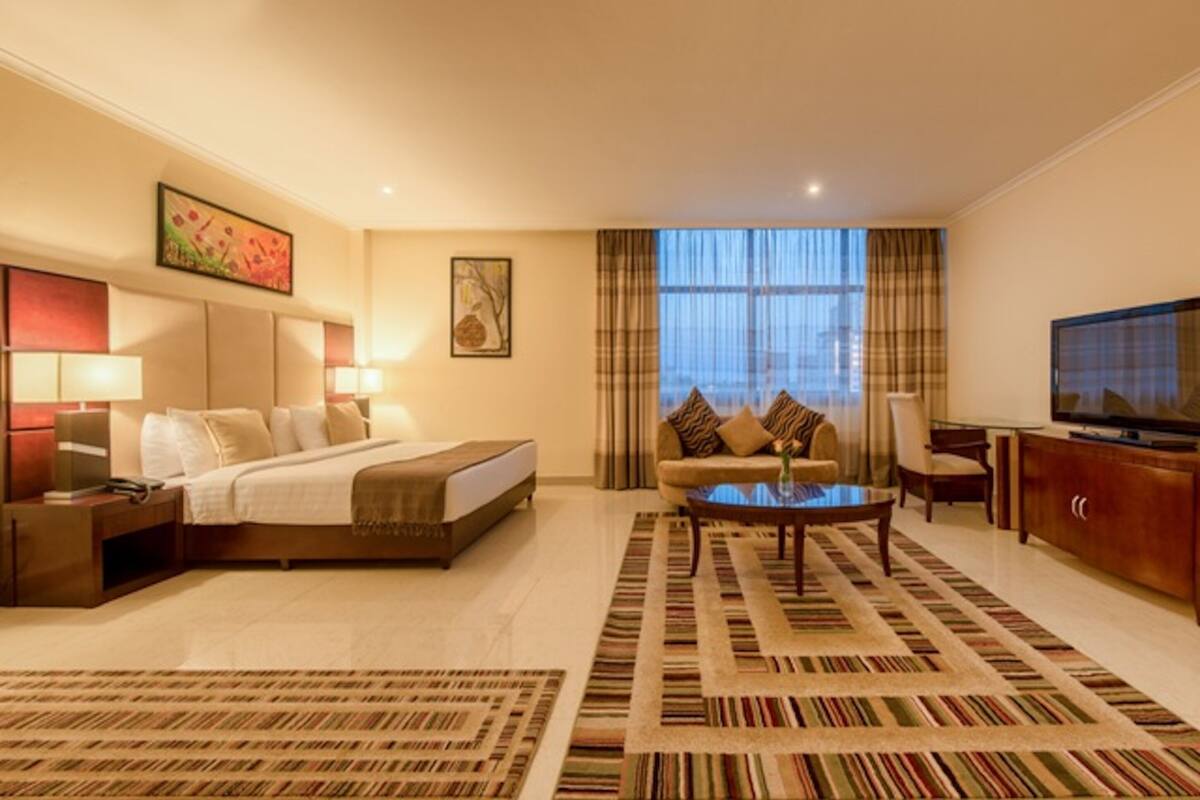 A hotel room with a bed, a sofa, a coffee table, and a TV.