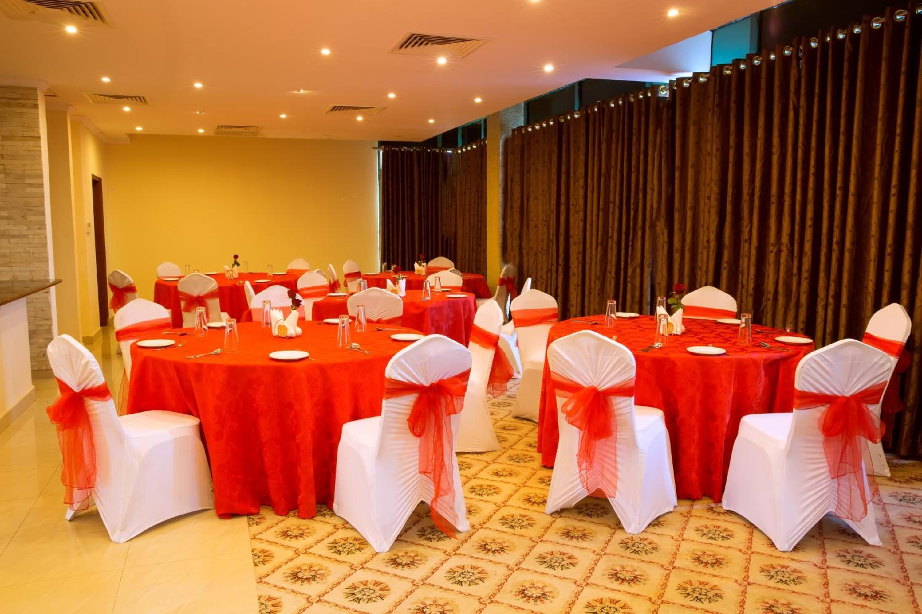 Un salón de conferencias con mesas redondas, sillas blancas con cintas rojas y una alfombra estampada.
