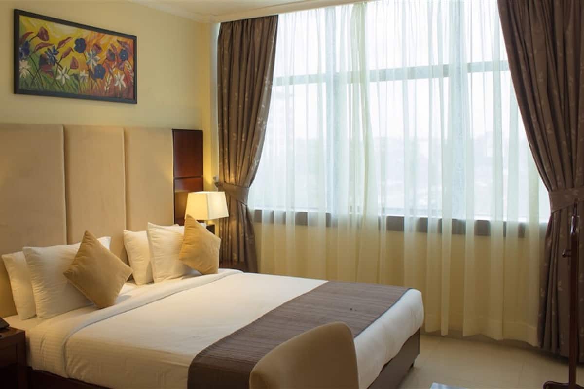 A hotel room with a large bed, two bedside lamps, a painting on the wall, and a window with curtains.