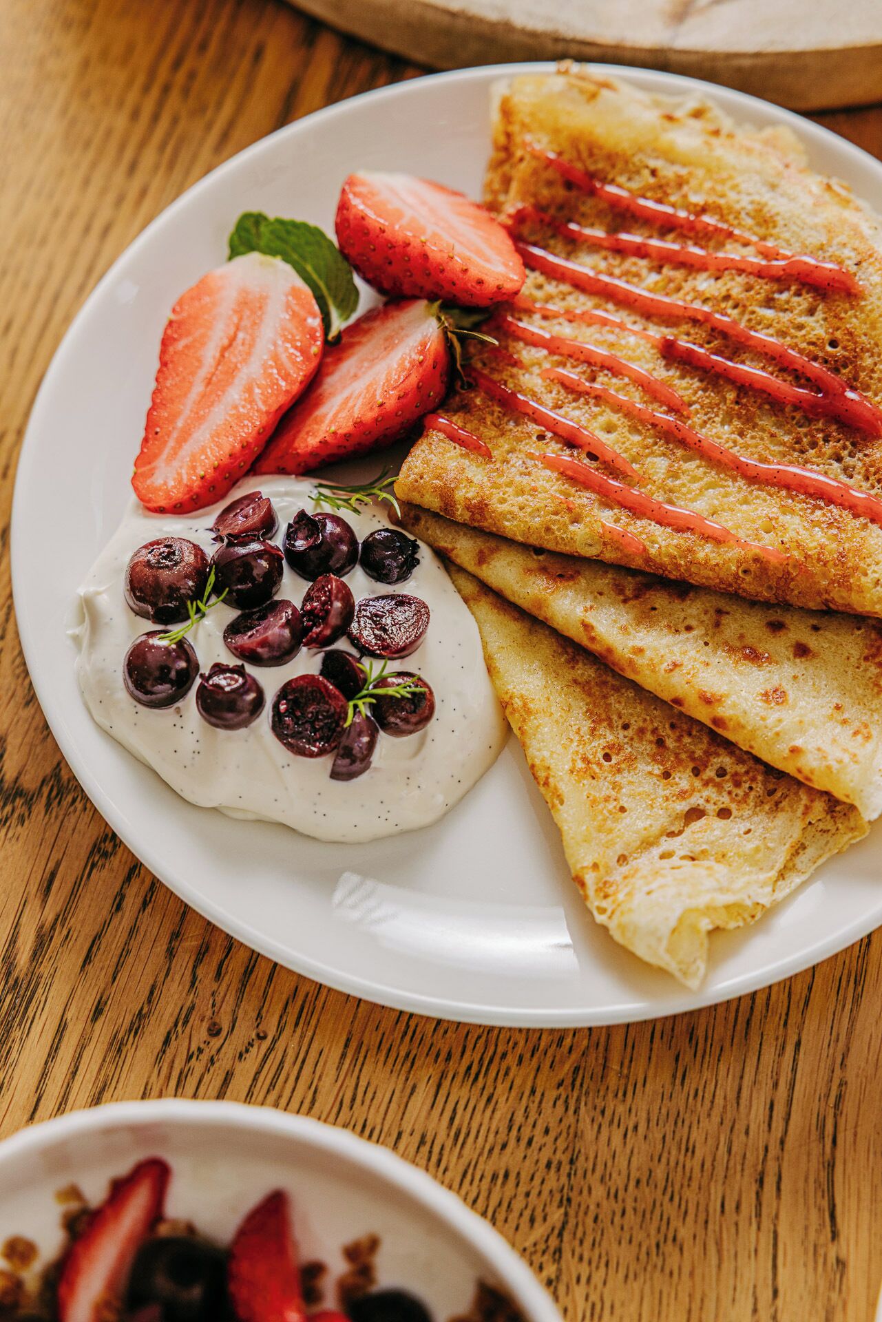 Ein Teller mit Crêpes, Erdbeeren und einem Klecks Sahne mit Beeren.