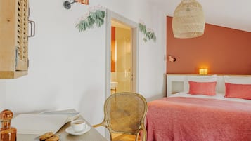 Un dormitori amb un llit, una cadira, una taula amb una tassa i galetes, una làmpada i una estanteria penjada a la paret.