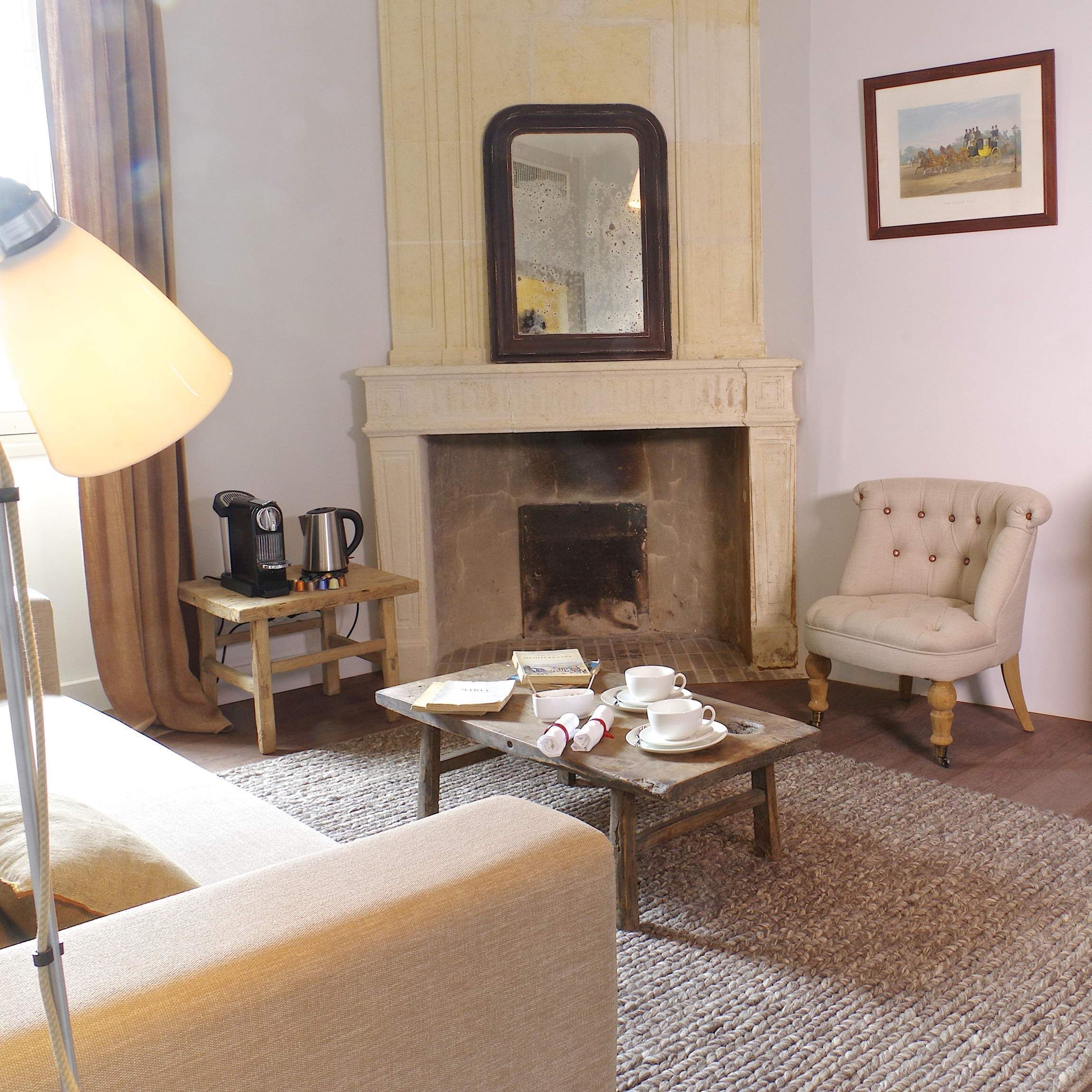 A living room with a fireplace, a coffee table with cups and saucers, a chair, and a lamp.