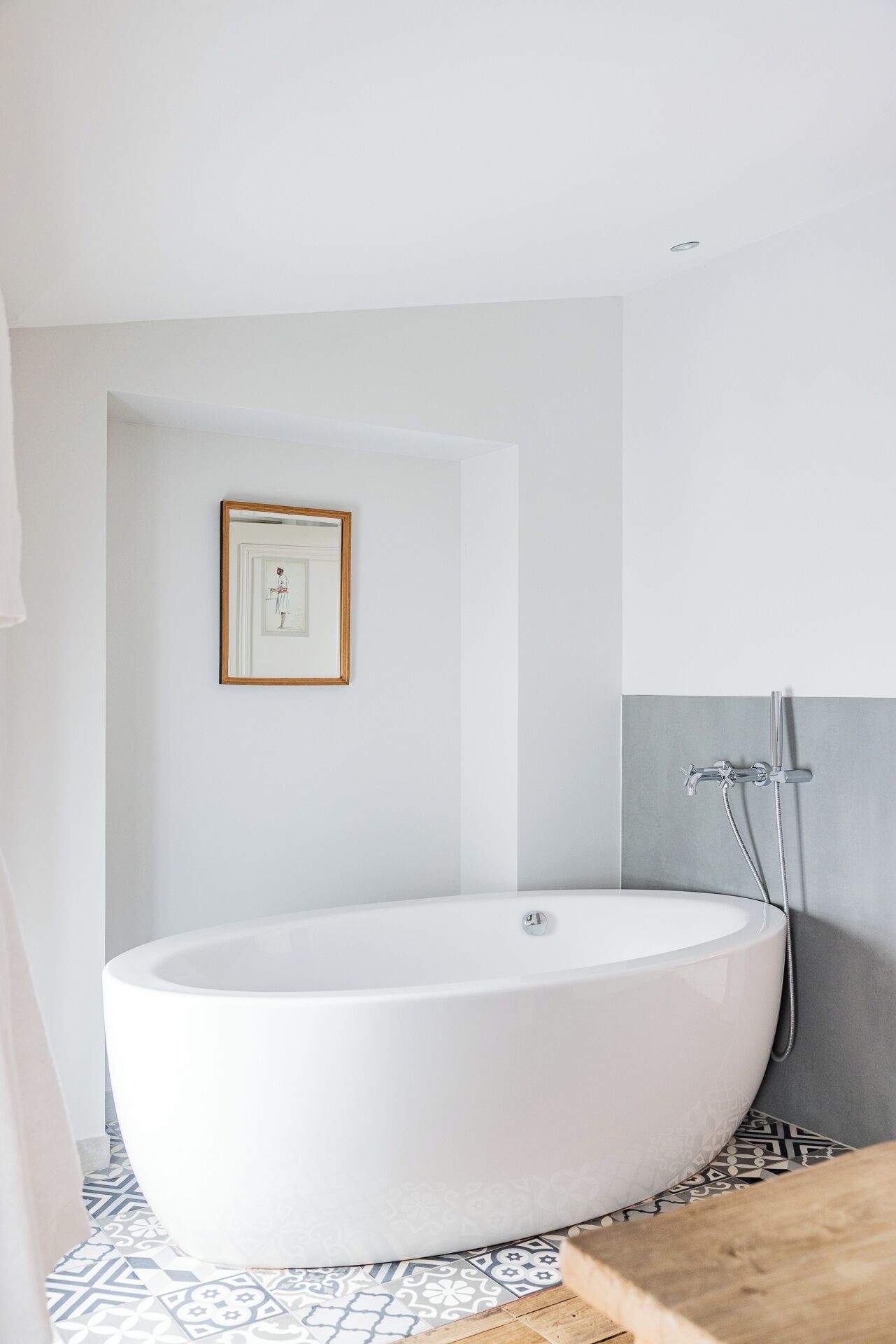 A modern bathroom with a freestanding bathtub, a framed picture on the wall, and a shower with a grey accent wall.