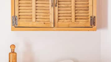 Un mueble de madera con dos puertas, una silla de mimbre, una taza blanca, un libro y una botella sobre una mesa.