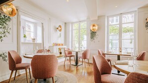Un comedor con mesas y sillas redondas, ventanas amplias y apliques decorativos.