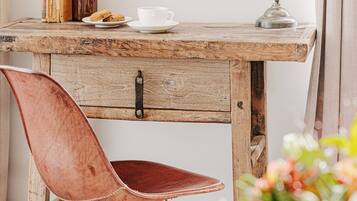 A rustic wooden desk with a vintage lamp, a leather chair, and a small table with a cup and cookies.