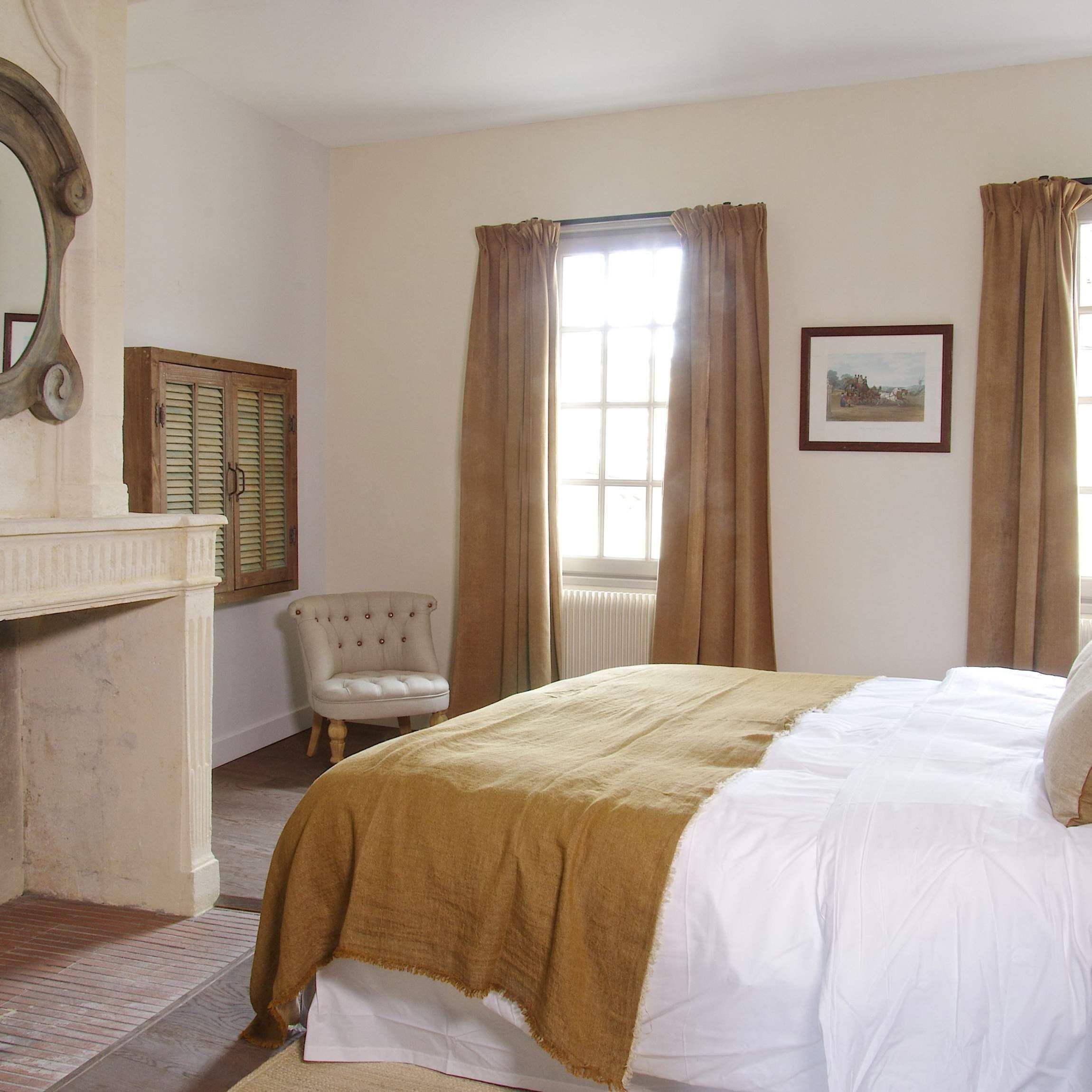 Un dormitorio con cama, una silla, chimenea y ventana con cortinas.