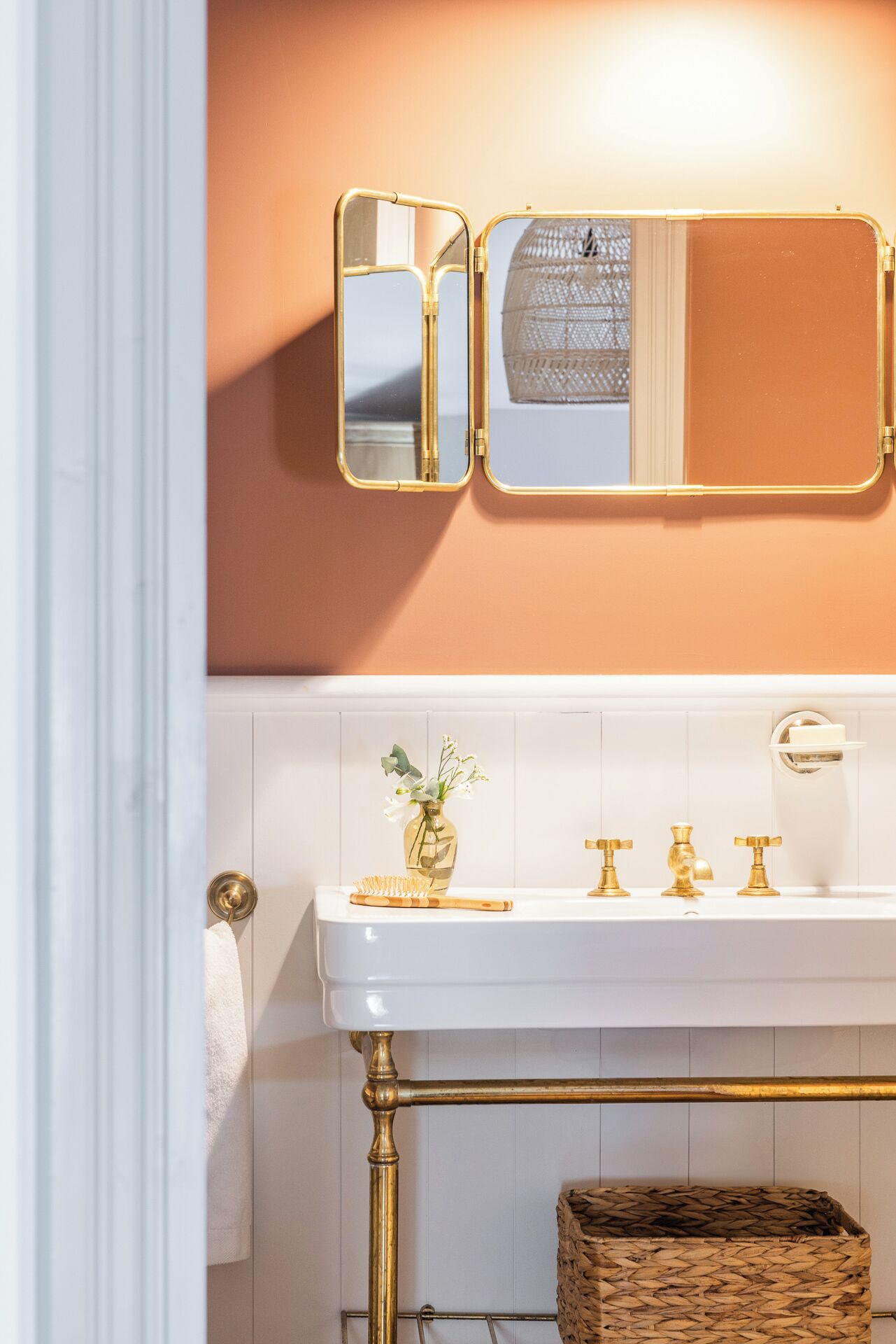 A bathroom with a white sink, gold fixtures, a mirror, and a woven basket.