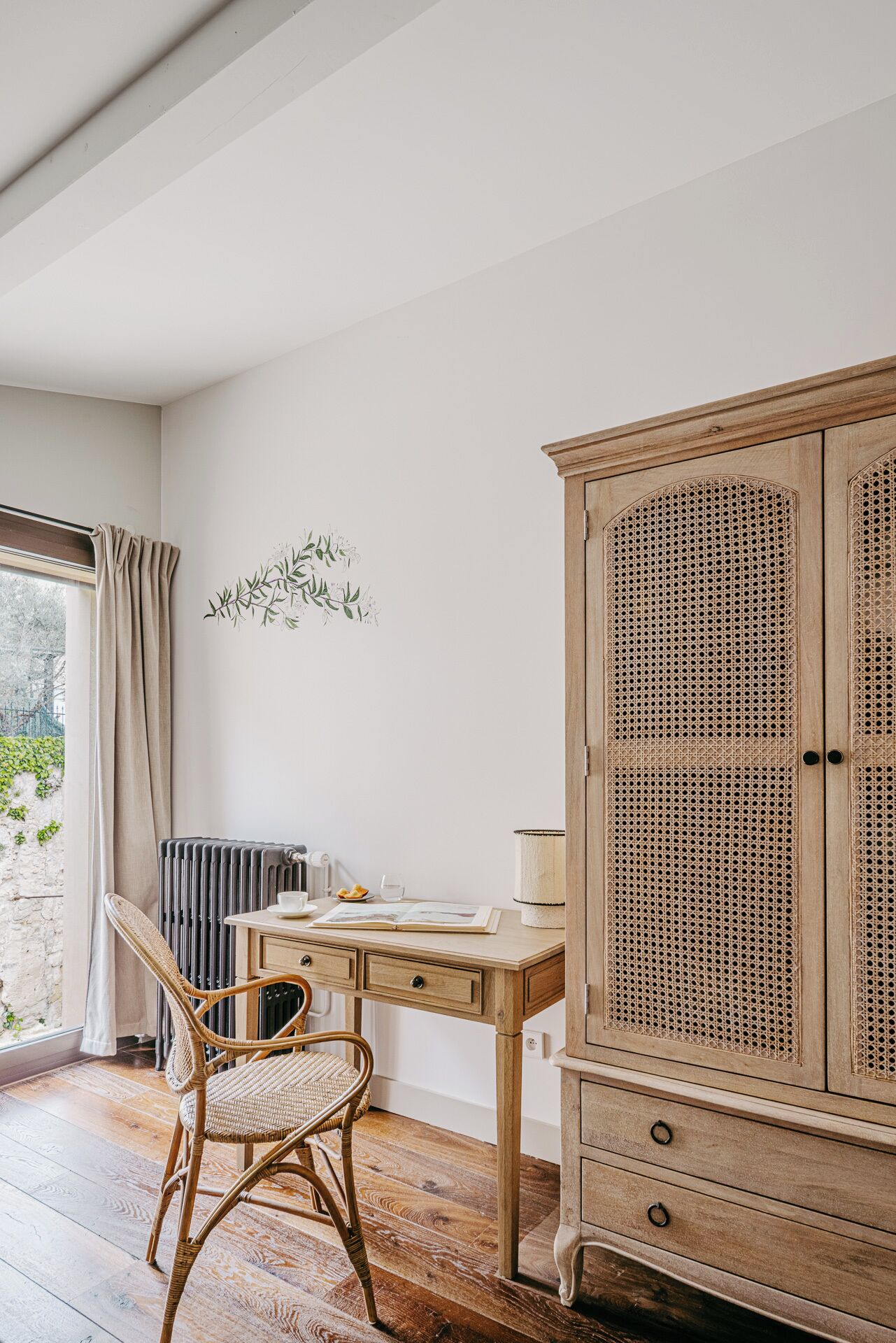 Um quarto com uma escrivaninha de madeira, cadeira de vime e aparador de rattan.