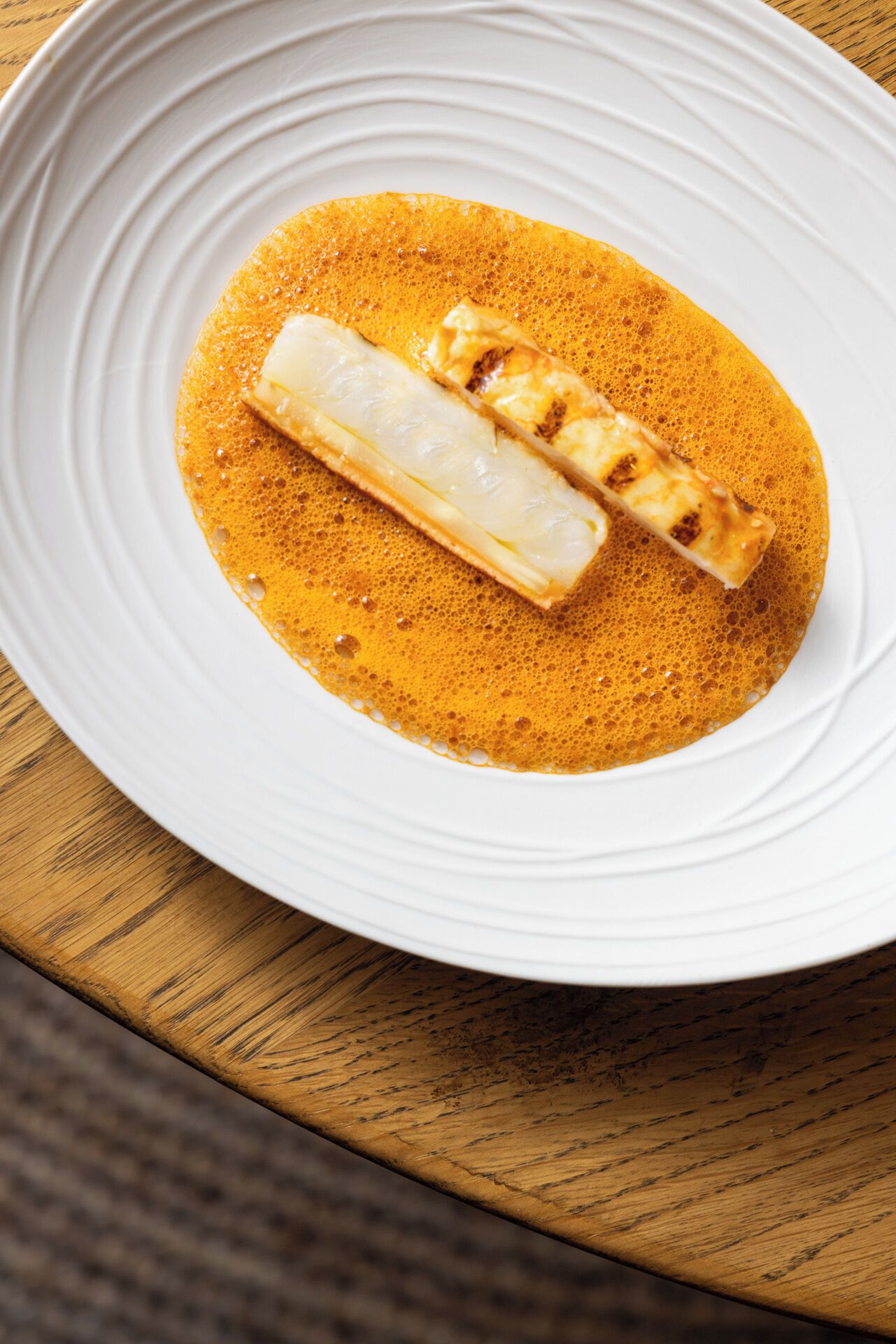 Une assiette blanche sur laquelle repose un morceau de poisson grillé, nappé d’une sauce orange.