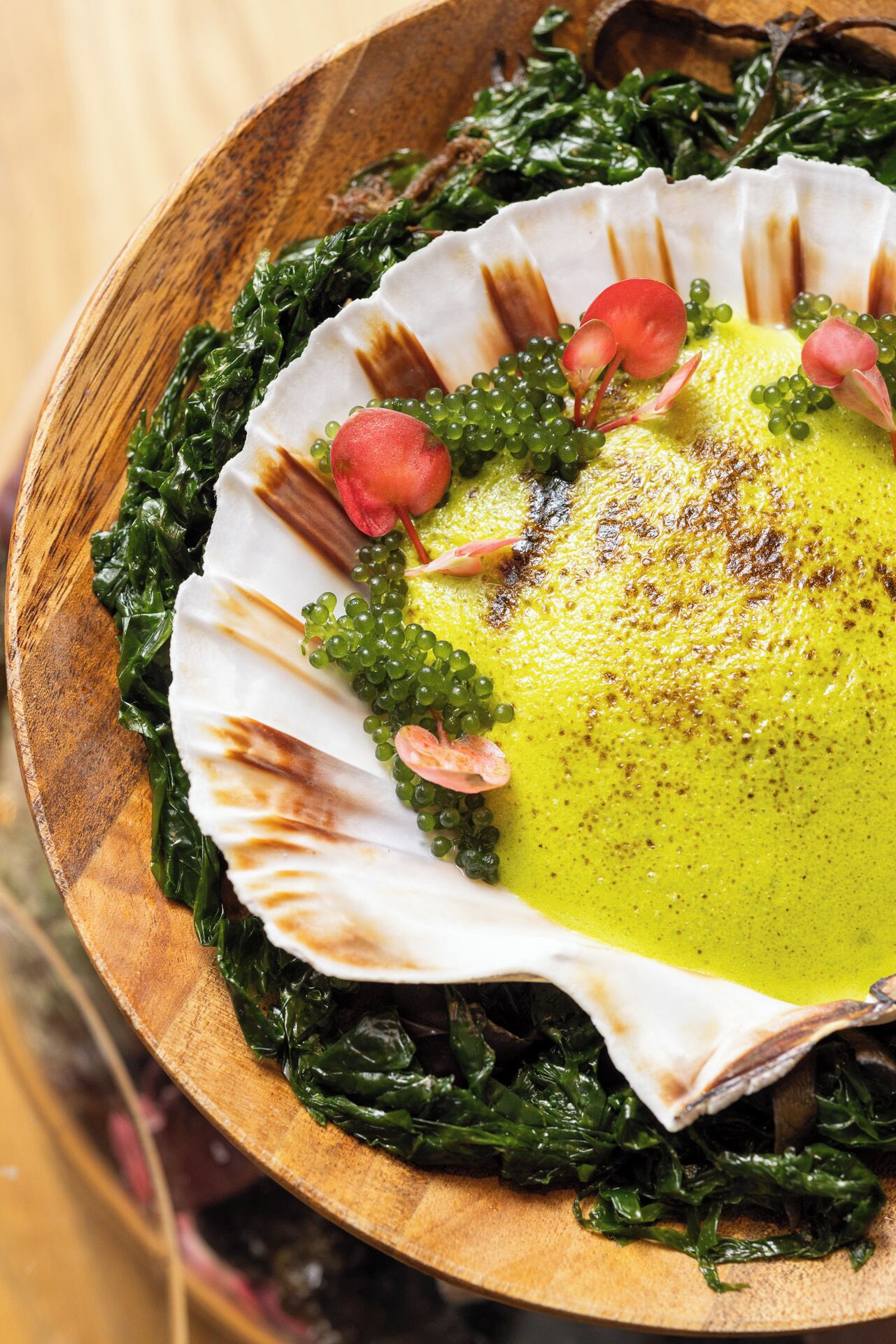 A dish with greens, a yellow sauce, and red elements on a wooden board.