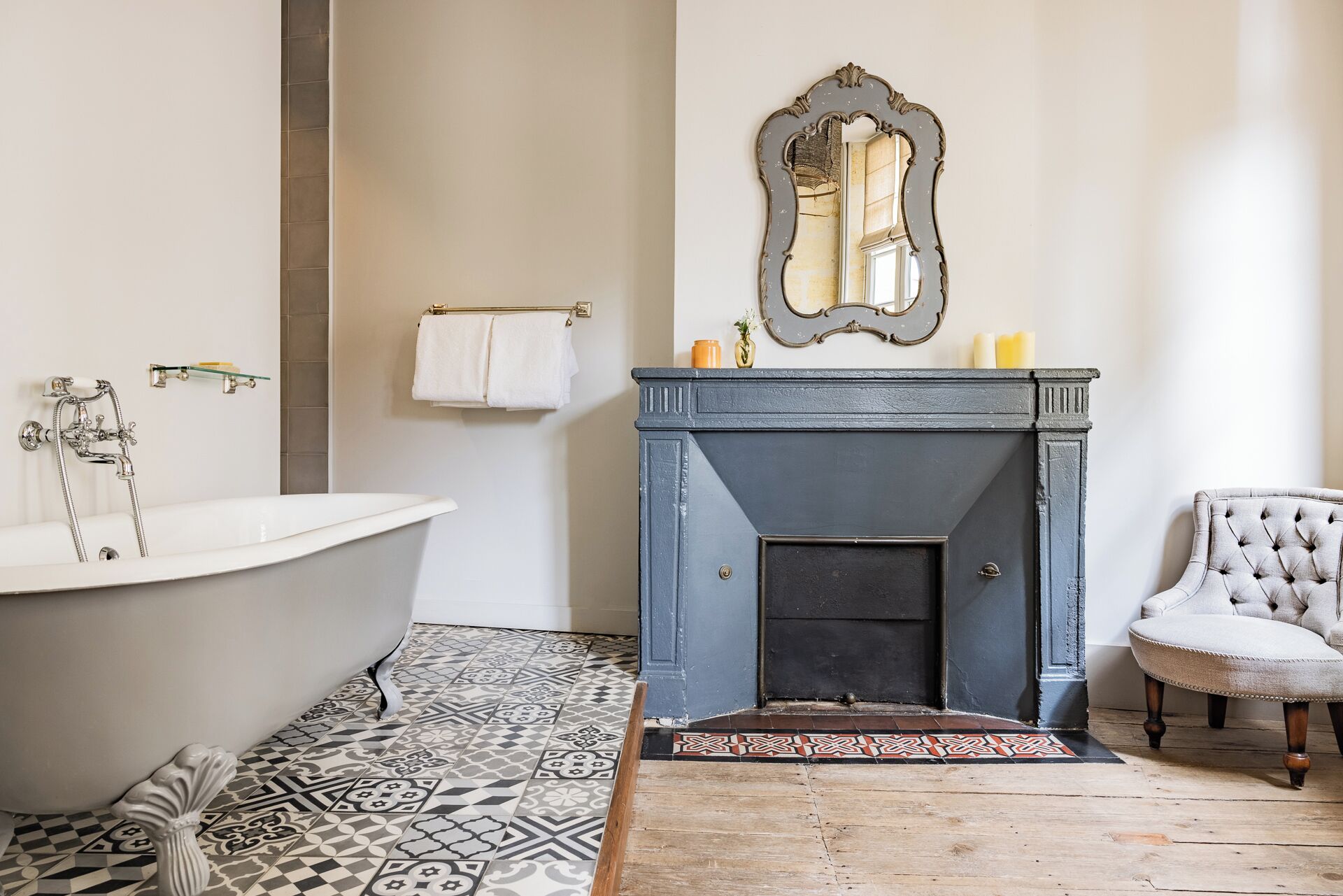 Une salle de bain avec une baignoire sur pieds, un miroir décoratif au-dessus d’une cheminée et un carrelage à motifs.