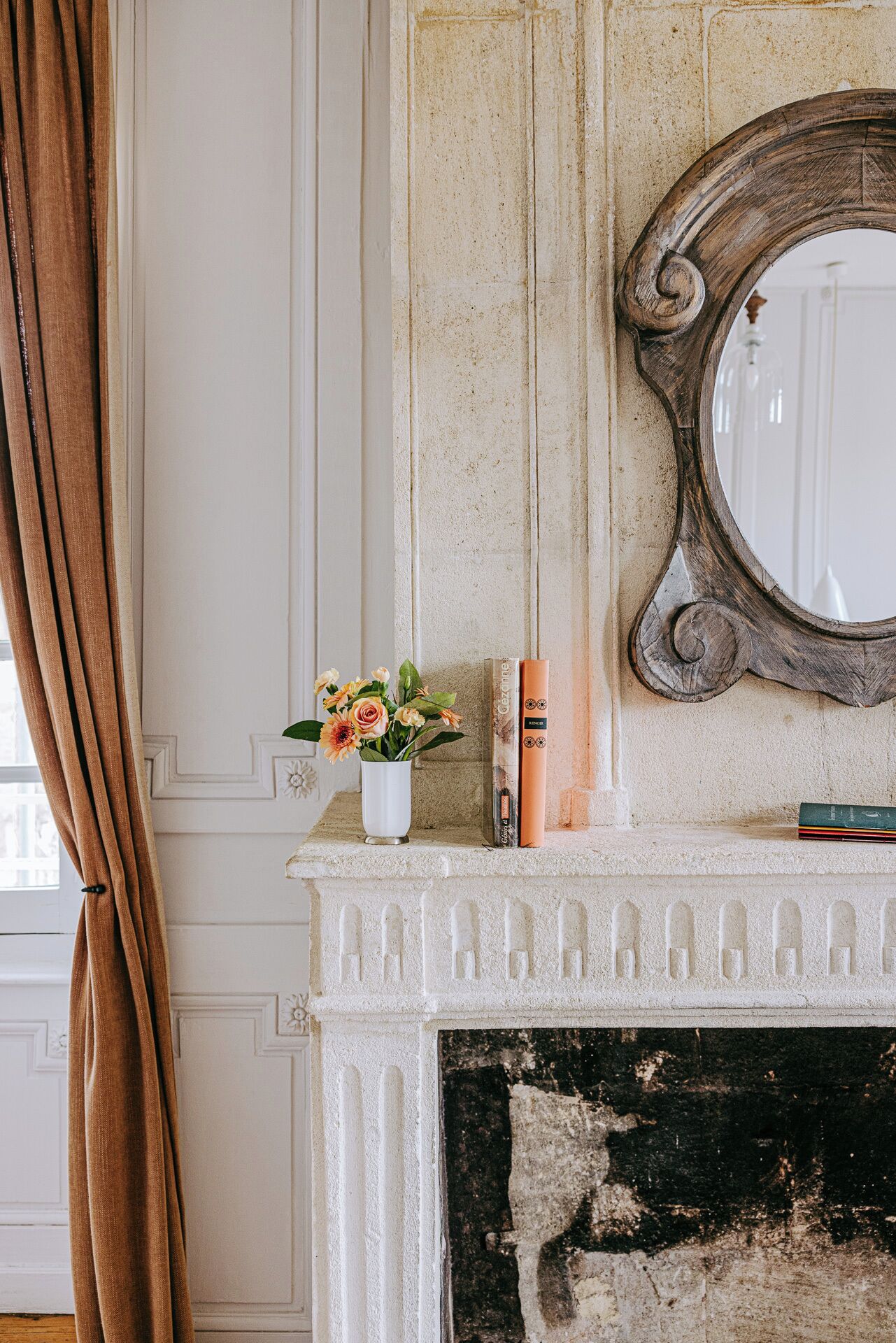 Une cheminée avec un manteau de couleur blanche, un miroir et un vase rempli de fleurs.