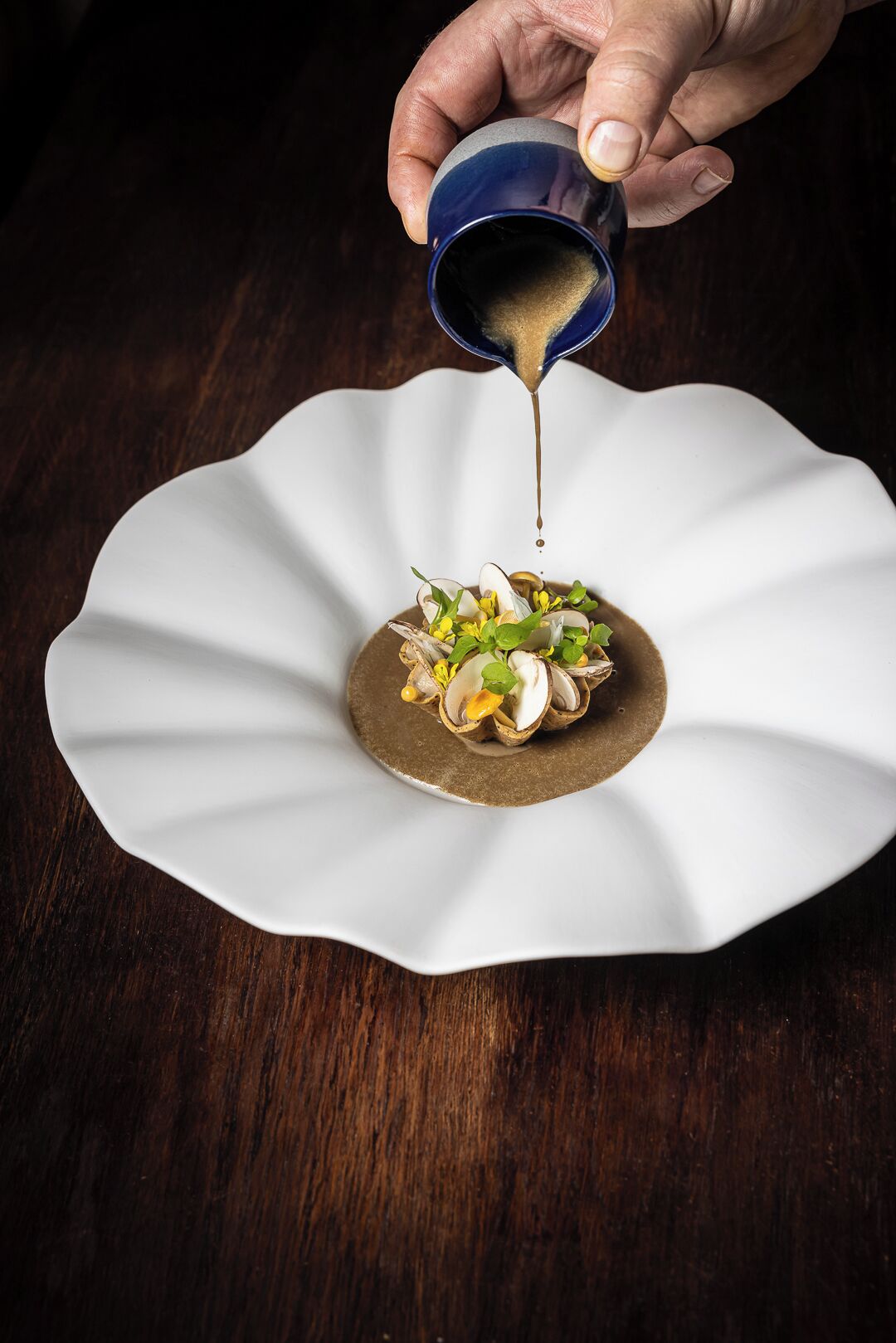 A hand pouring a sauce over a dish on a white plate.