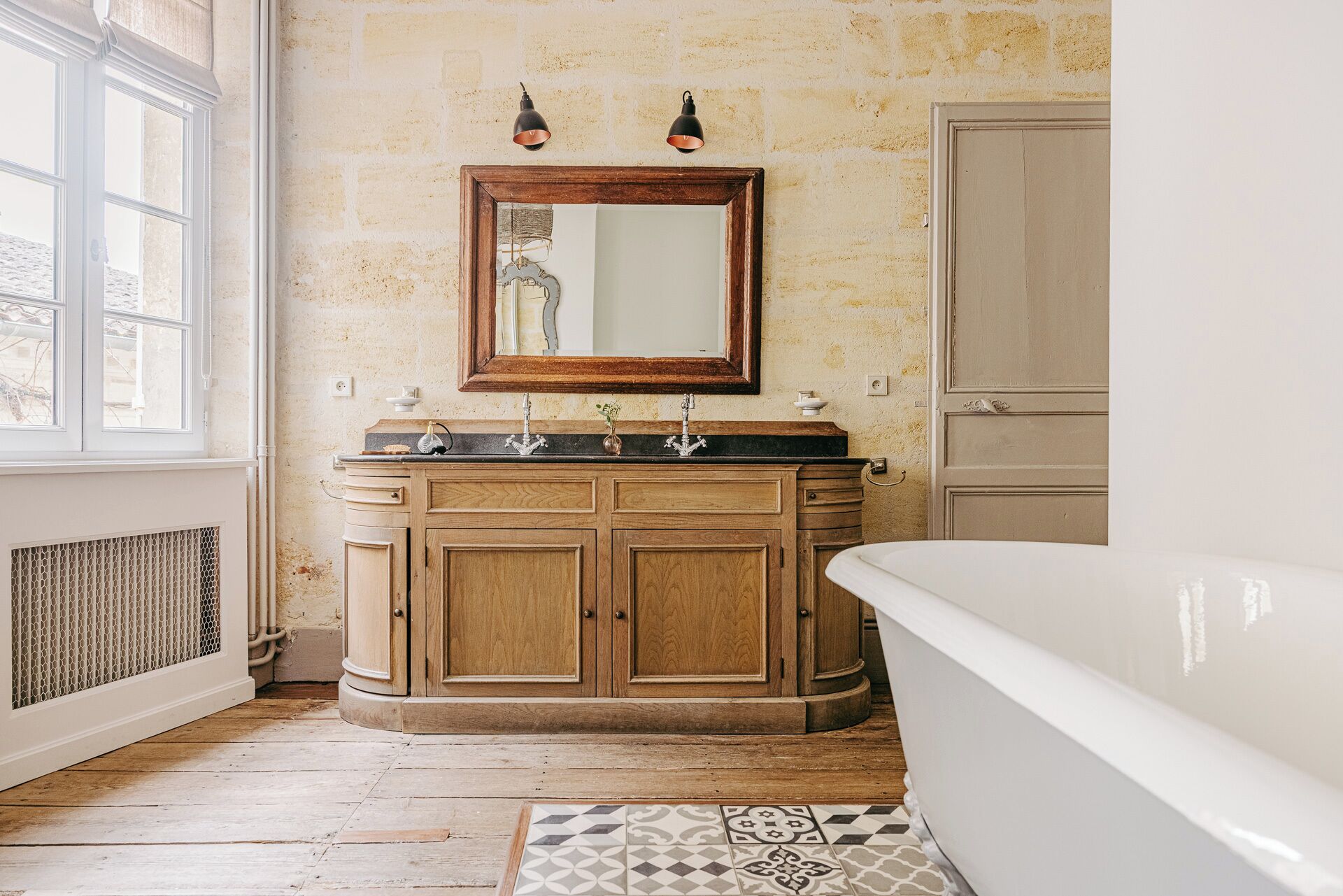 Une salle de bain avec un meuble-lavabo en bois, un grand miroir, deux appliques murales et une baignoire.