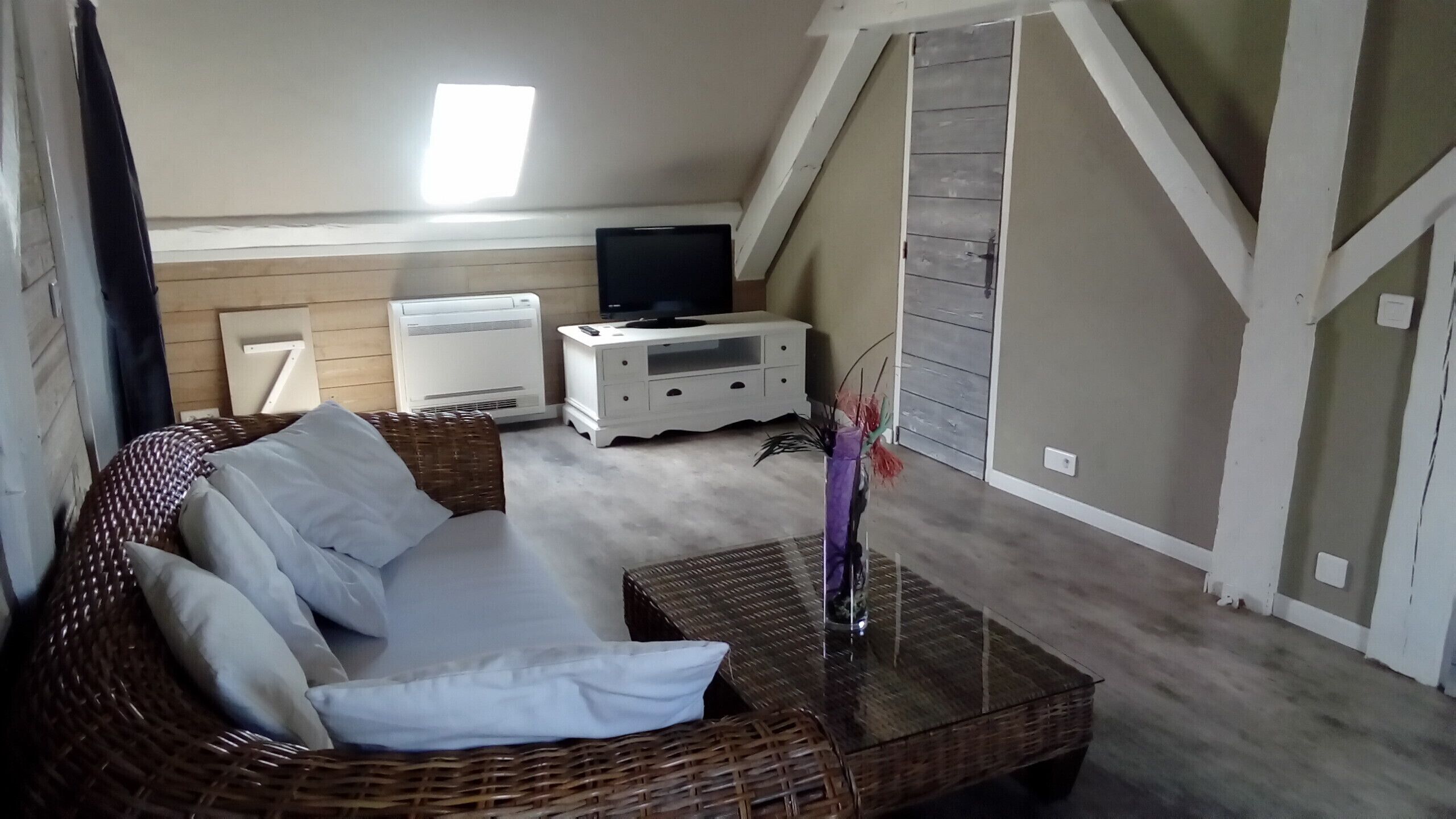 A cozy living room with a wicker sofa, a glass coffee table, and a white TV stand.