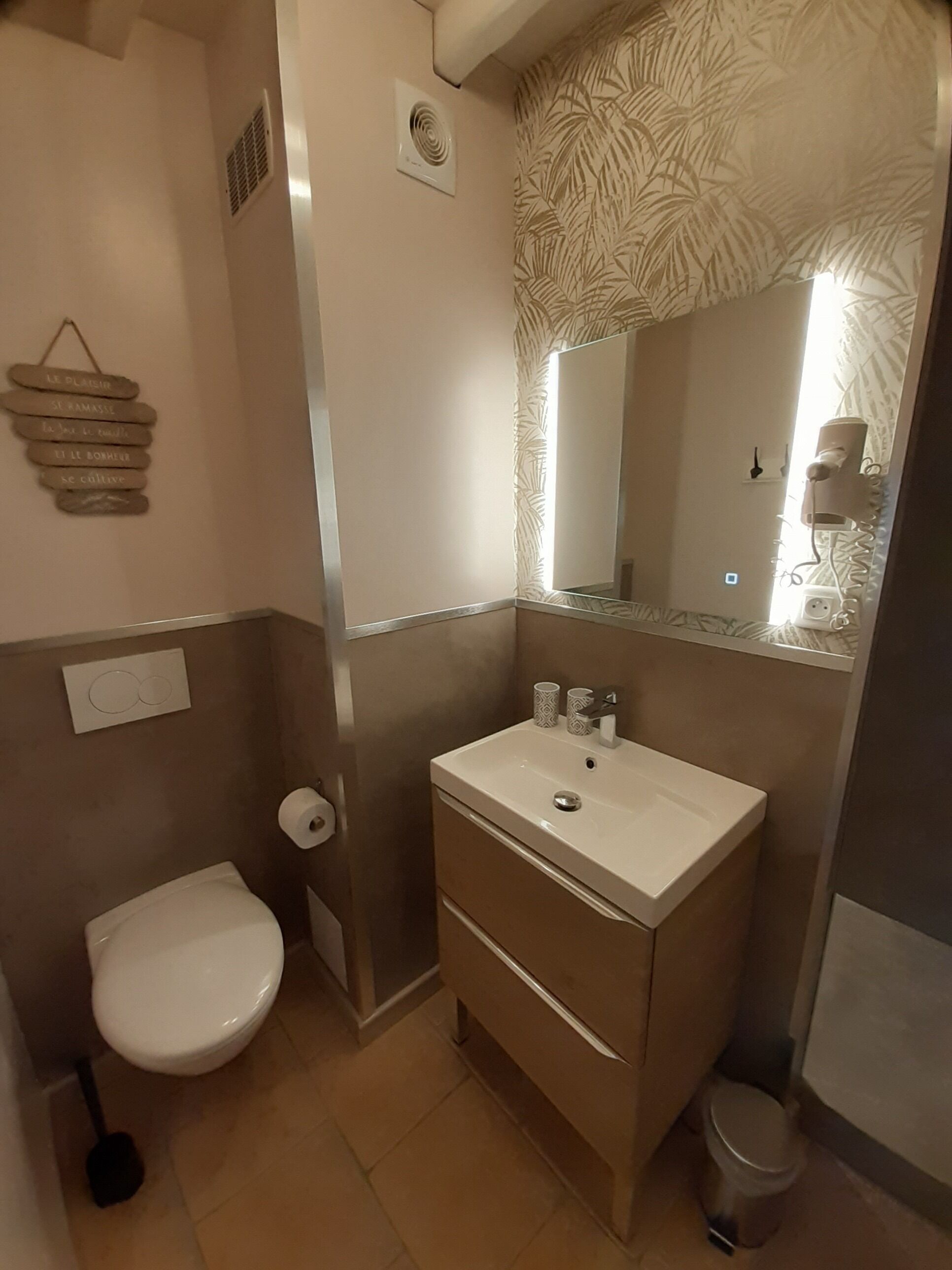 Une salle de bain avec un lavabo blanc, des toilettes et un miroir au-dessus du lavabo.