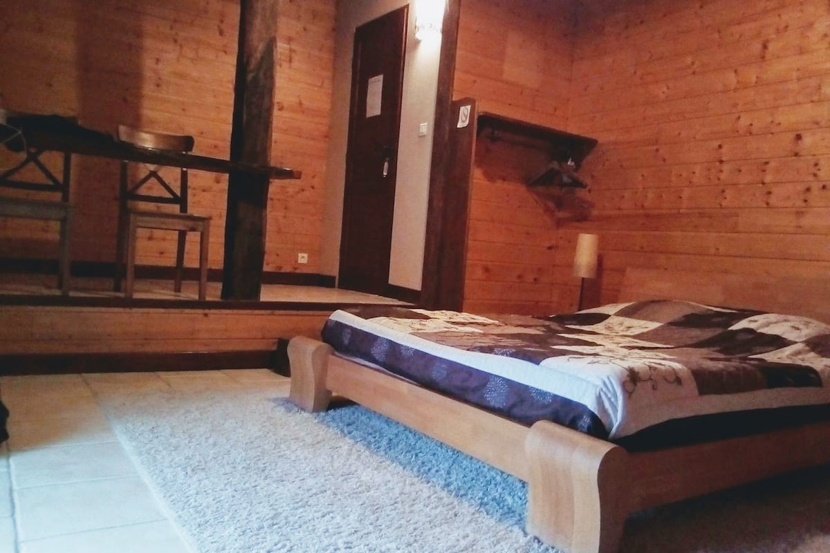 A wooden cabin bedroom with a bed, a small table, and a chair.