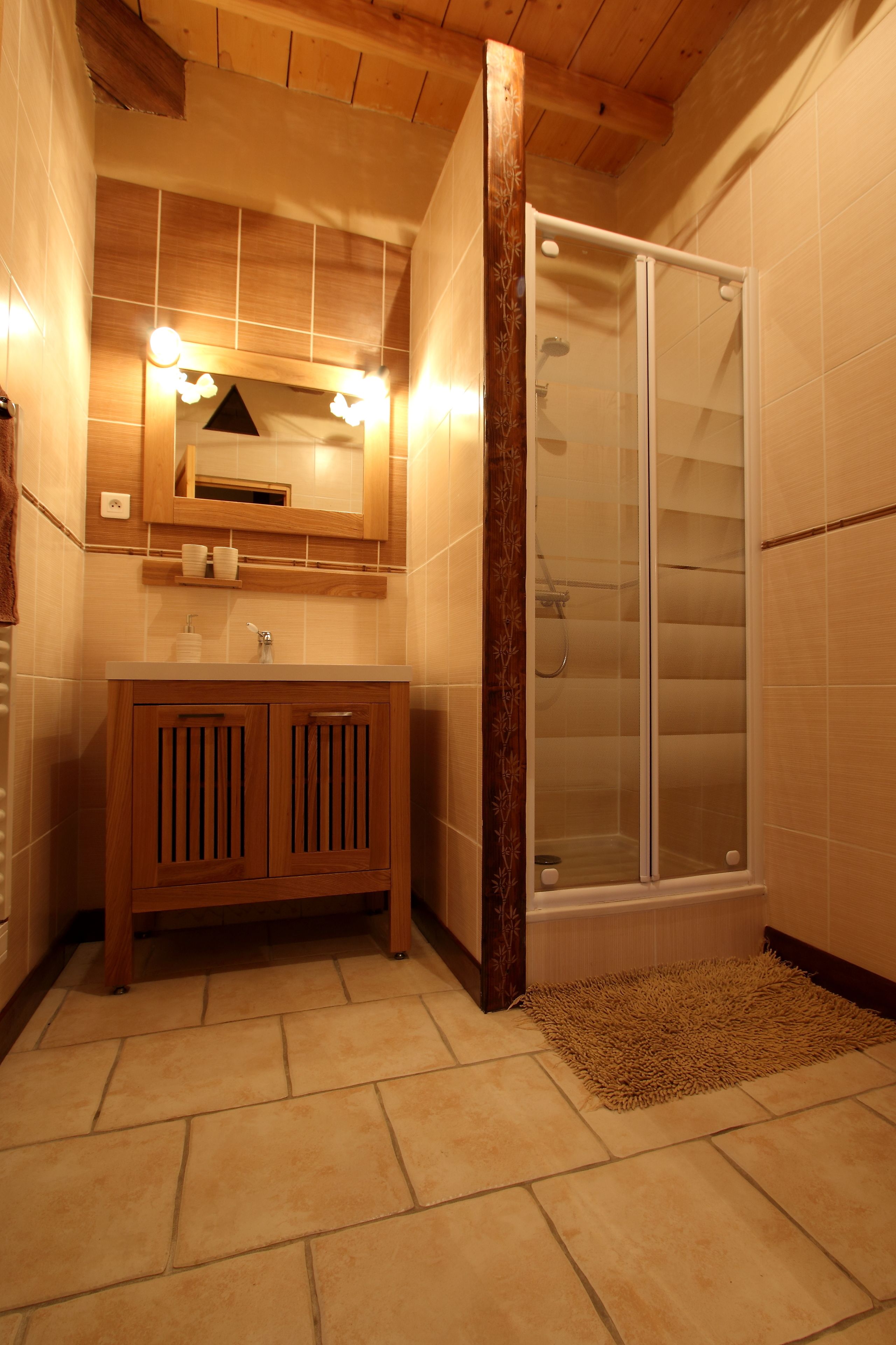 Un baño con tocador de madera, cabina de ducha con mampara de vidrio y piso de baldosas.
