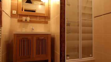 Un baño con tocador de madera, cabina de ducha con mampara de vidrio y piso de baldosas.