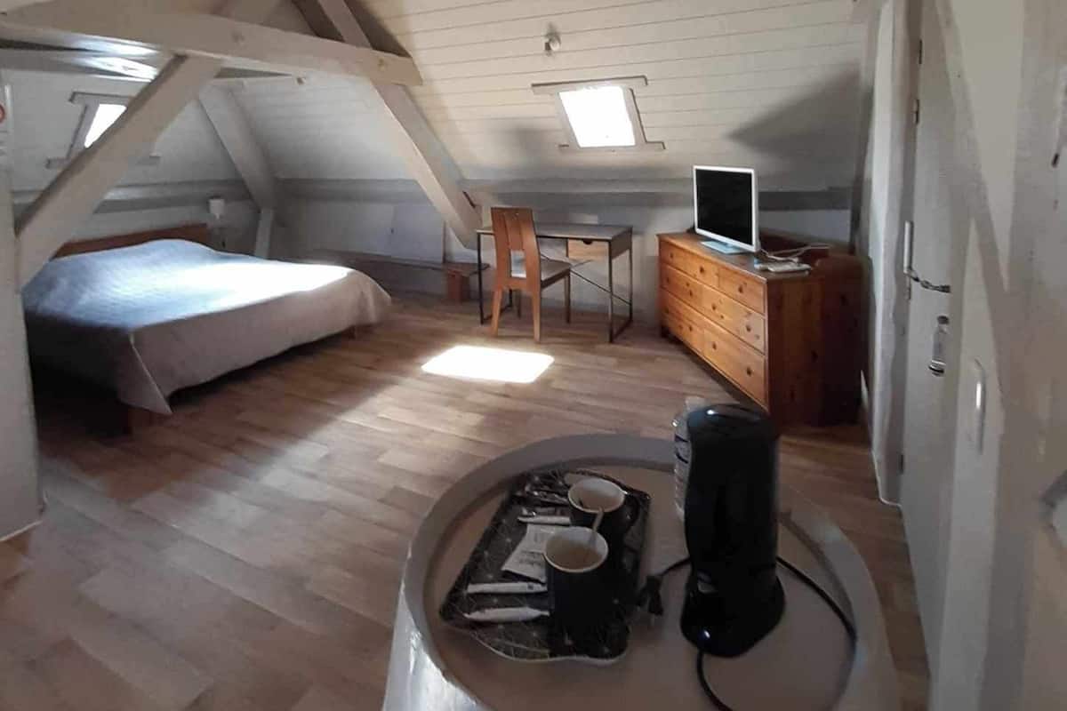 A small attic bedroom with a sloped ceiling, a bed, a desk with a chair, a dresser, and a television.
