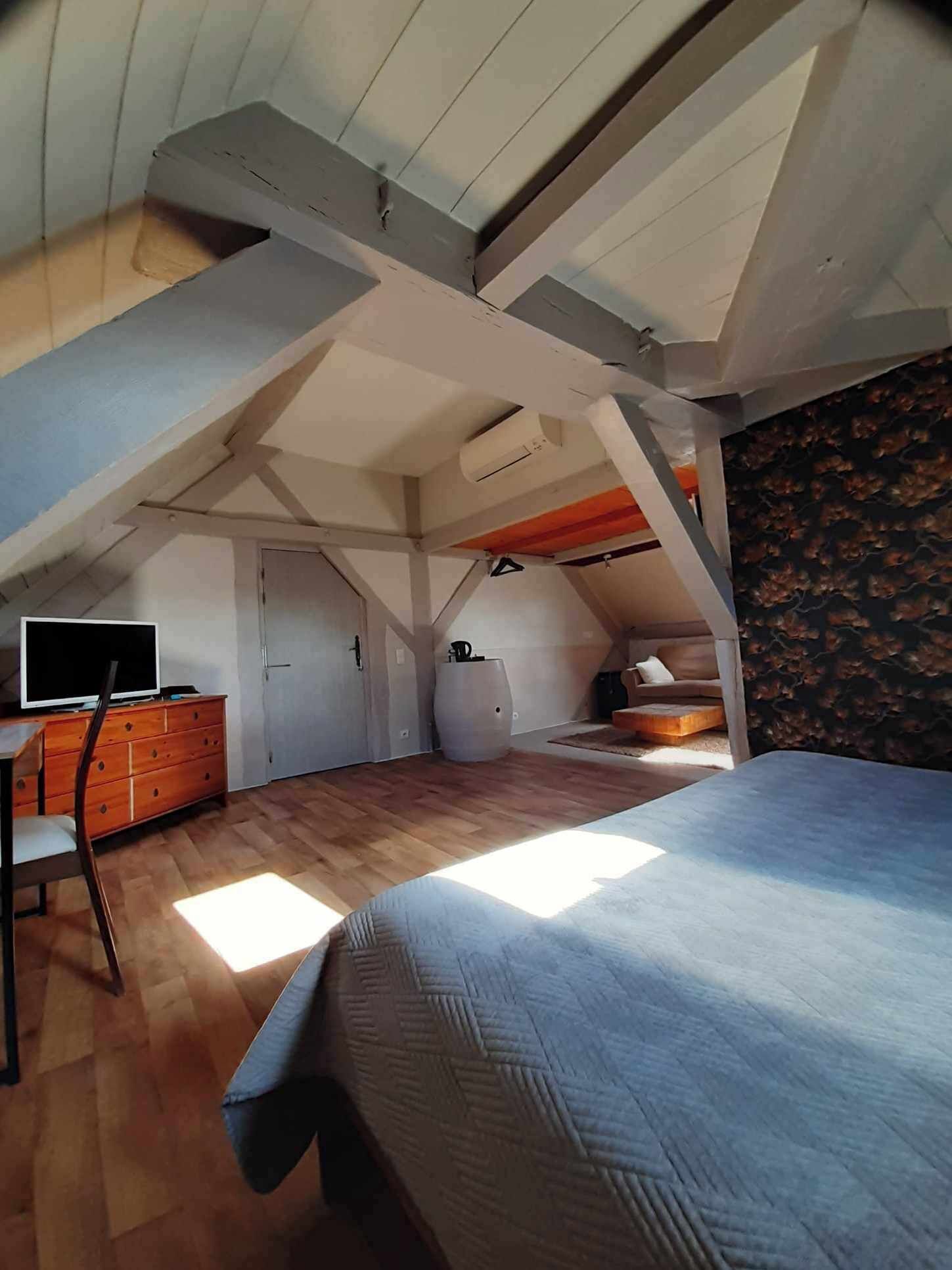 A bedroom with a sloped ceiling, a bed, a dresser, a television, and a large window allowing natural light.