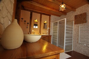 Un baño con tocador de madera, dos lavamanos, un jarrón grande y zona de ducha.
