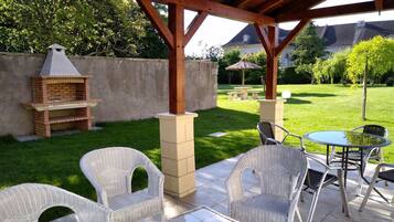 Un patio al aire libre con mobiliario de mimbre, una parrilla de ladrillo y un pilar de piedra.