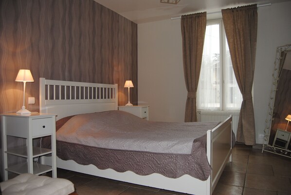 Un dormitorio con una cama individual, dos mesitas de noche con lámparas, un radiador, una ventana con cortinas y un espejo en la pared.