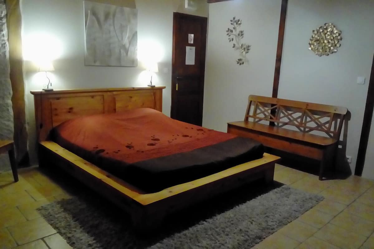A bedroom with a wooden bed, a bench, a stone wall, and a door.