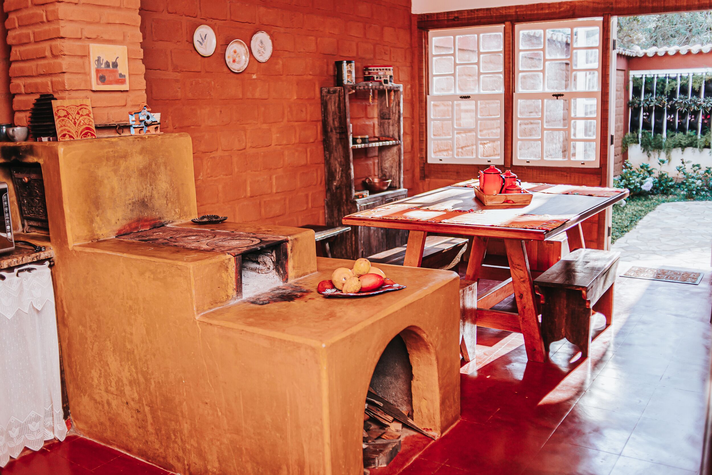 A rustic kitchen with a brick wall, wooden furniture, and a window with a view of greenery.