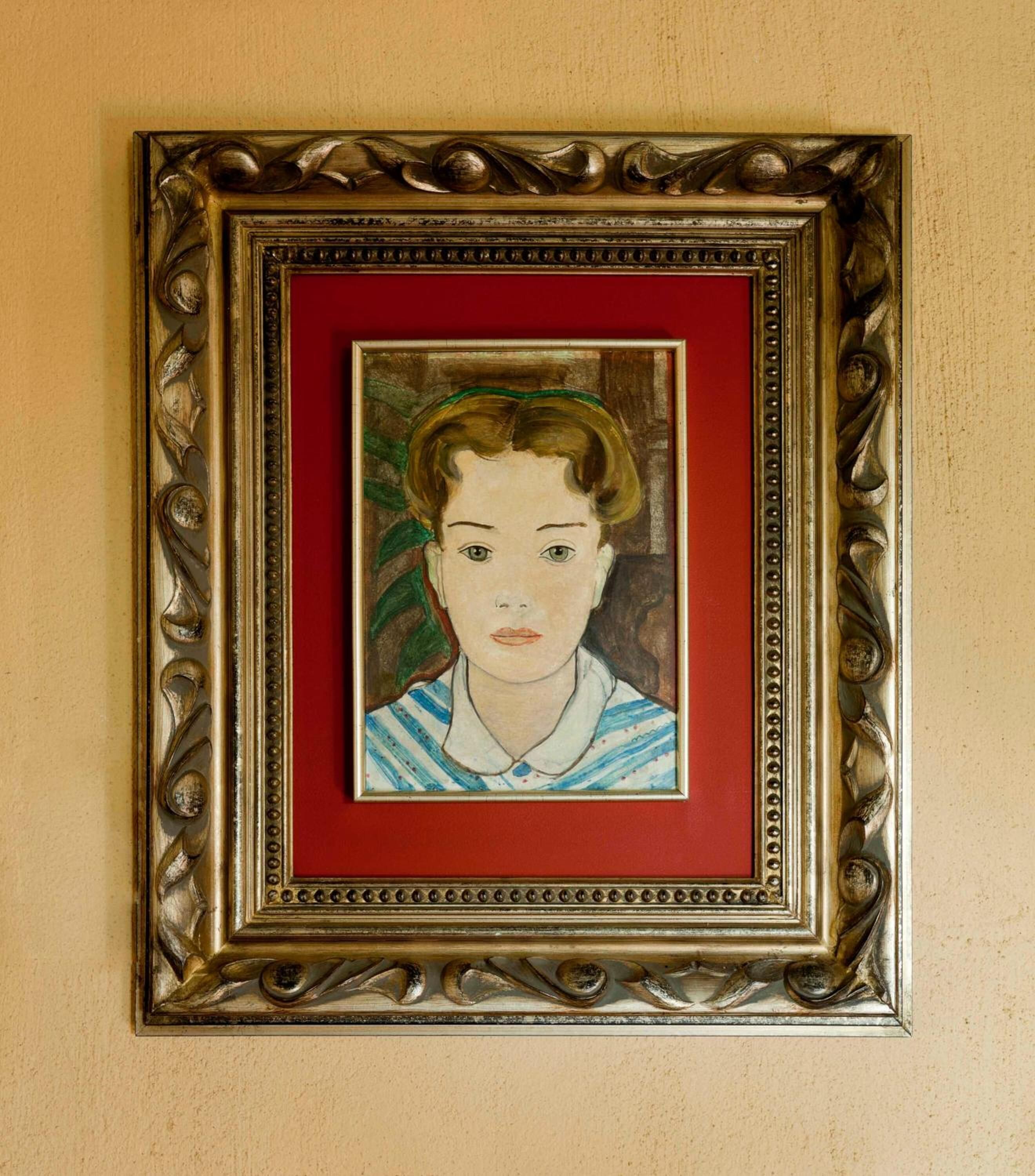 Uma obra de arte emoldurada com moldura dourada e borda vermelha, fixada numa parede bege.