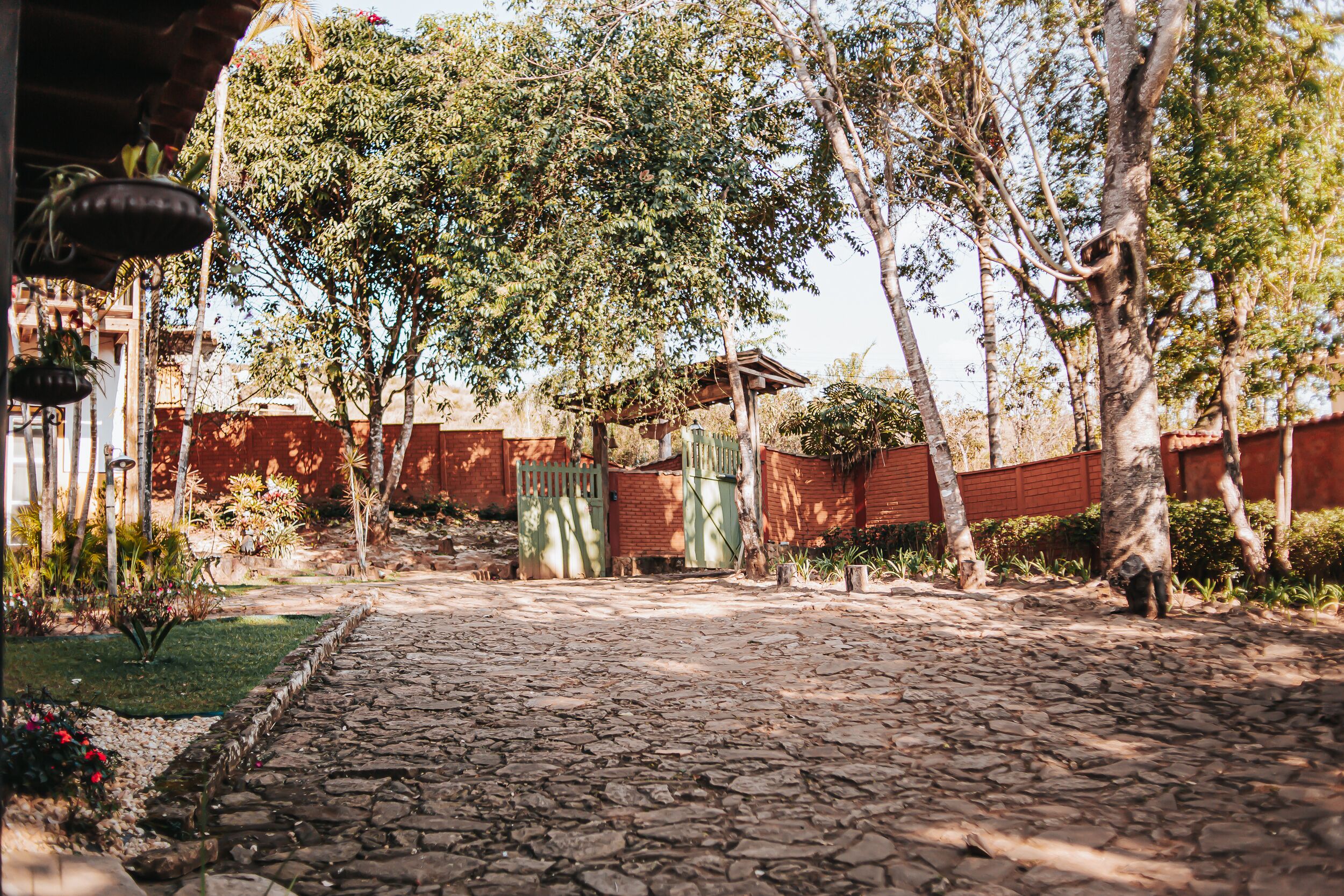 A stone-paved courtyard with a brick wall, trees, and a small wooden structure.