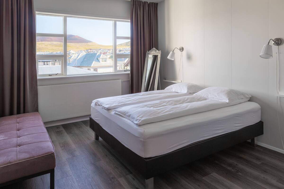 Une chambre à coucher avec un lit, un banc, une grande fenêtre et un miroir.