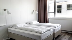 A room with two beds, a window with curtains, and wall-mounted lamps. - Guesthouse Hamar (Vestmannaeyjar)