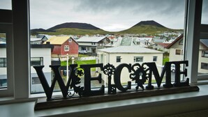 A window with a 'WELCOME' sign and a view of houses and a hill in the background. - Guesthouse Hamar (Vestmannaeyjar)