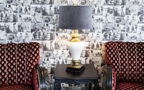 A room with a patterned sofa set, a table with a lamp, and a wall covered with black and white photographs. - Guesthouse Hamar (Vestmannaeyjar)